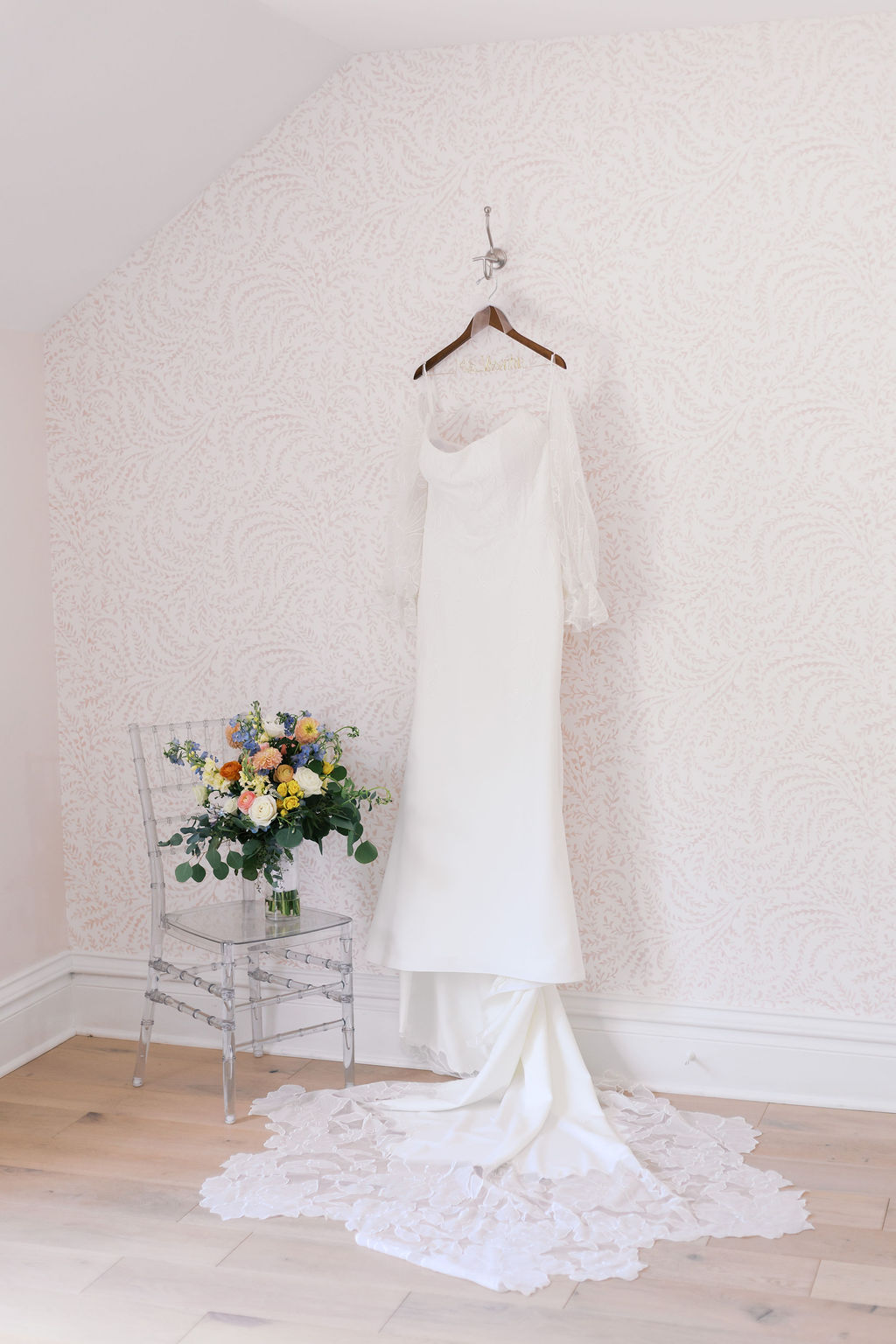 White bridal gown hanging next to chair with bouquet