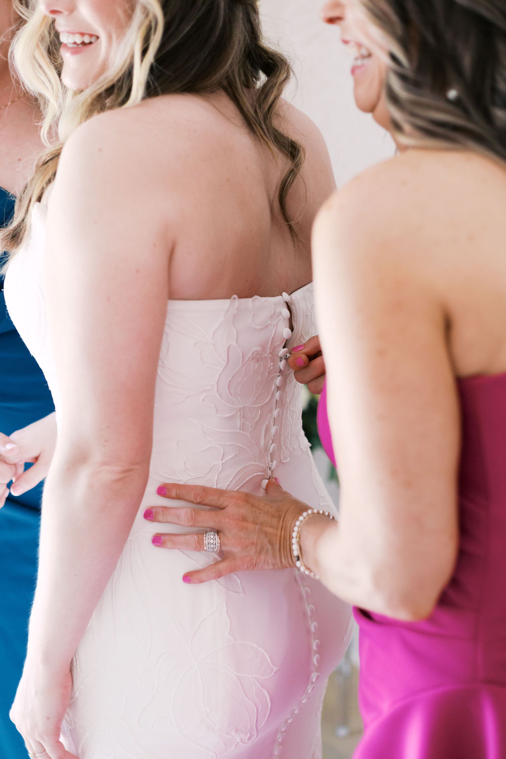 bride getting zipped into her dress by bridesmaid in pink dress