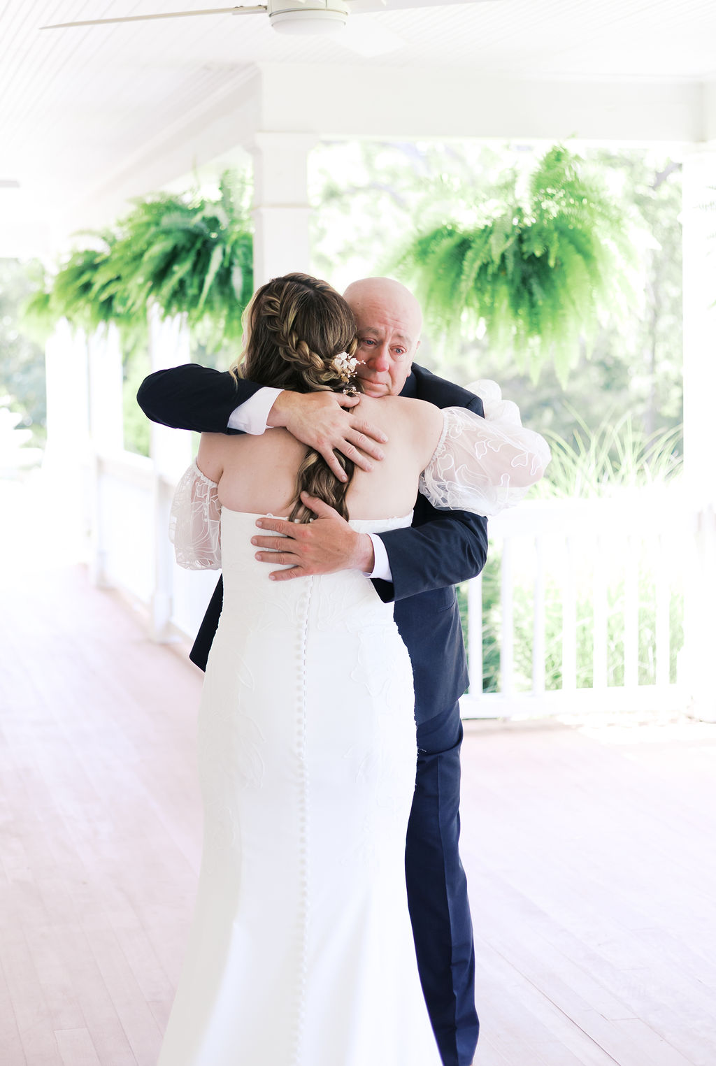 father and bride hugging on a porch with hanging ferns