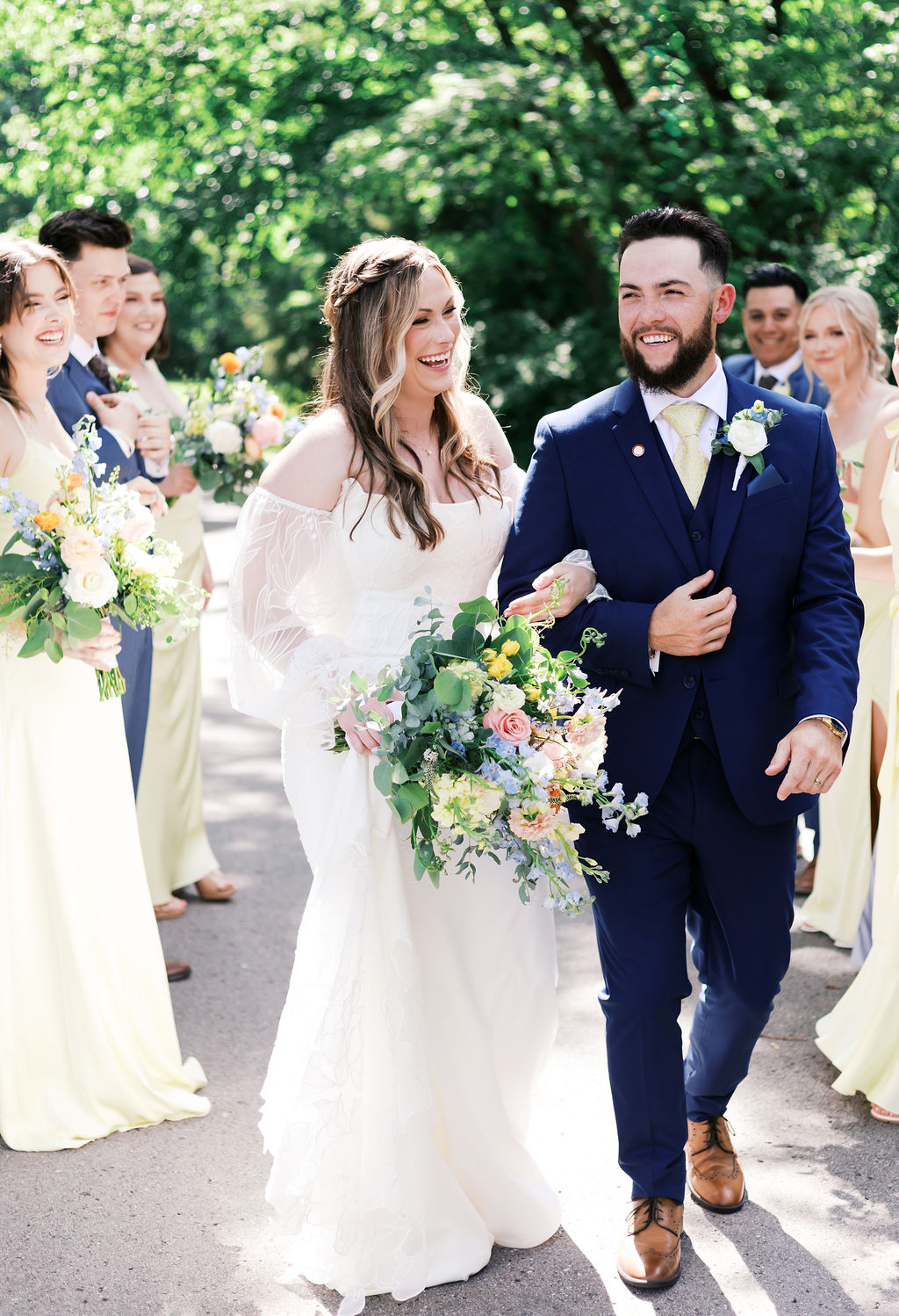 bride and groom walking arm in arm with bridal party looking on