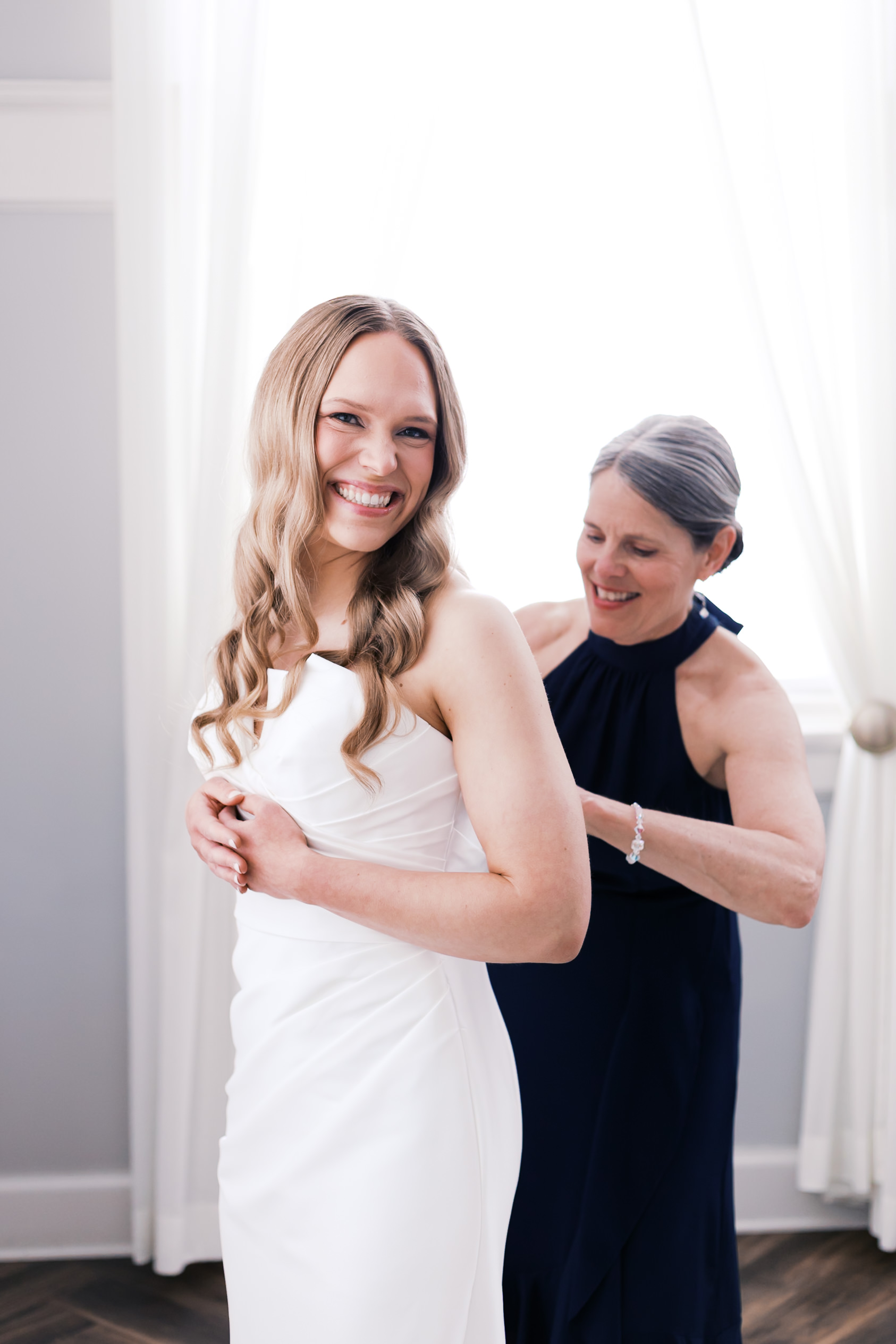 Bride smiling as woman buttons her dress