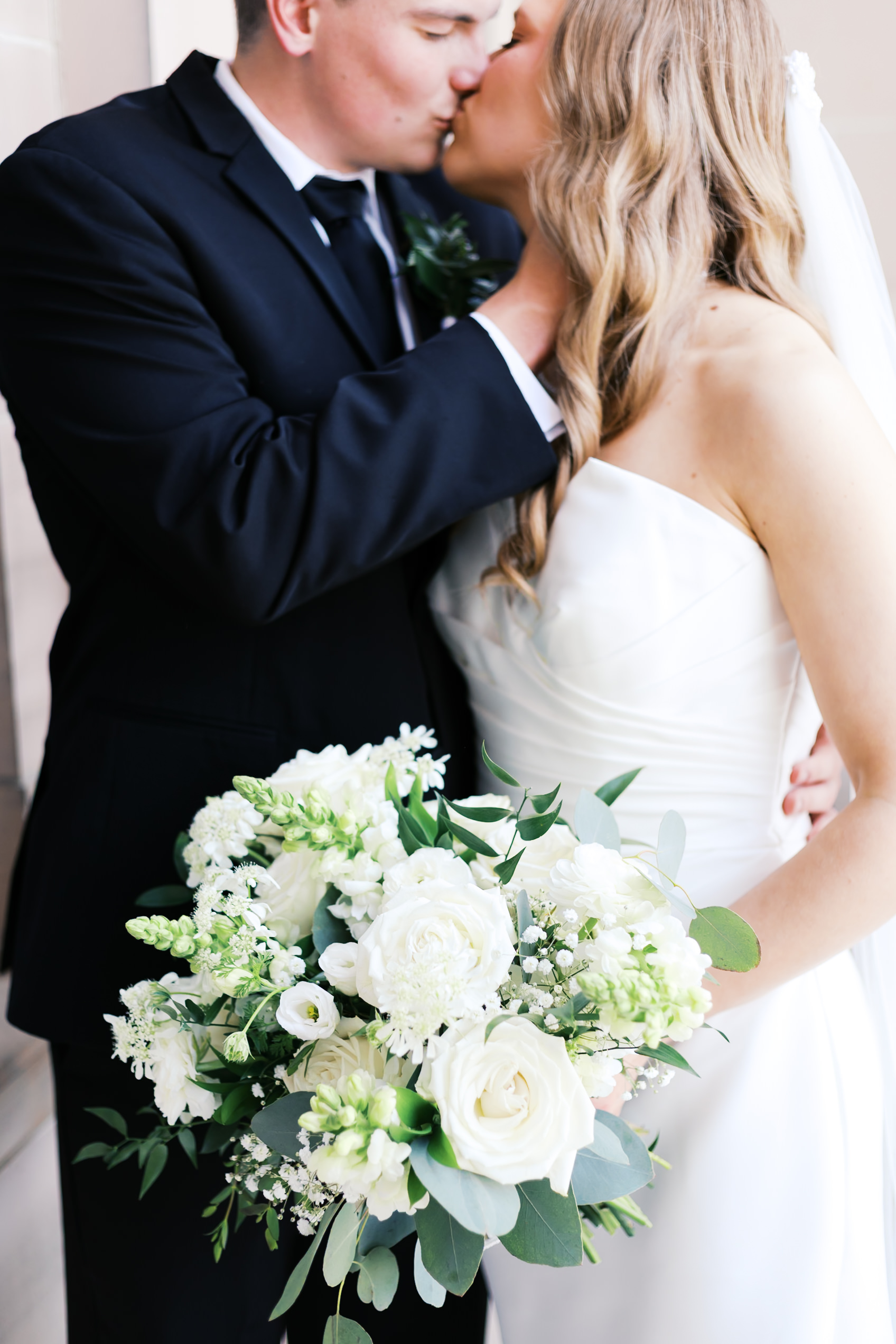 Close up kissing portrait of bride & groom with green and white bouquet