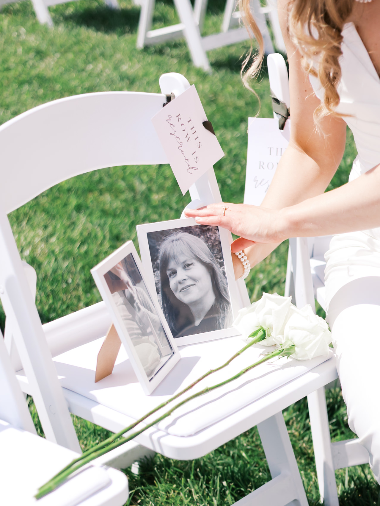 Close up of ceremony chair with framed photos of family and two white roses