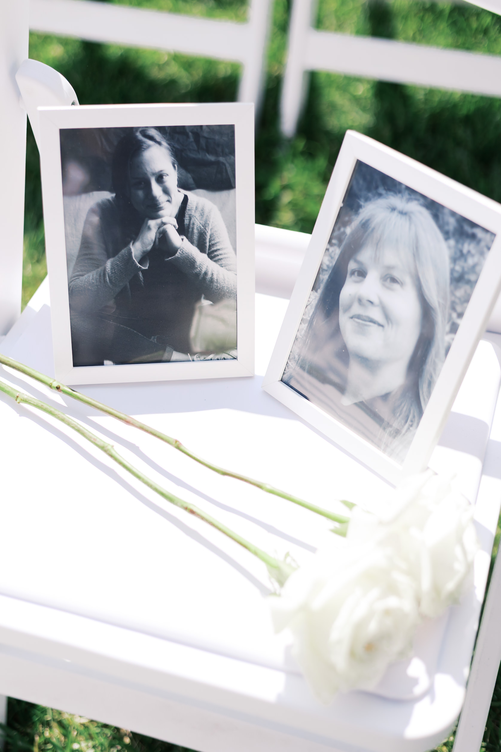 Close up of ceremony chair with framed photos of two women and two white roses