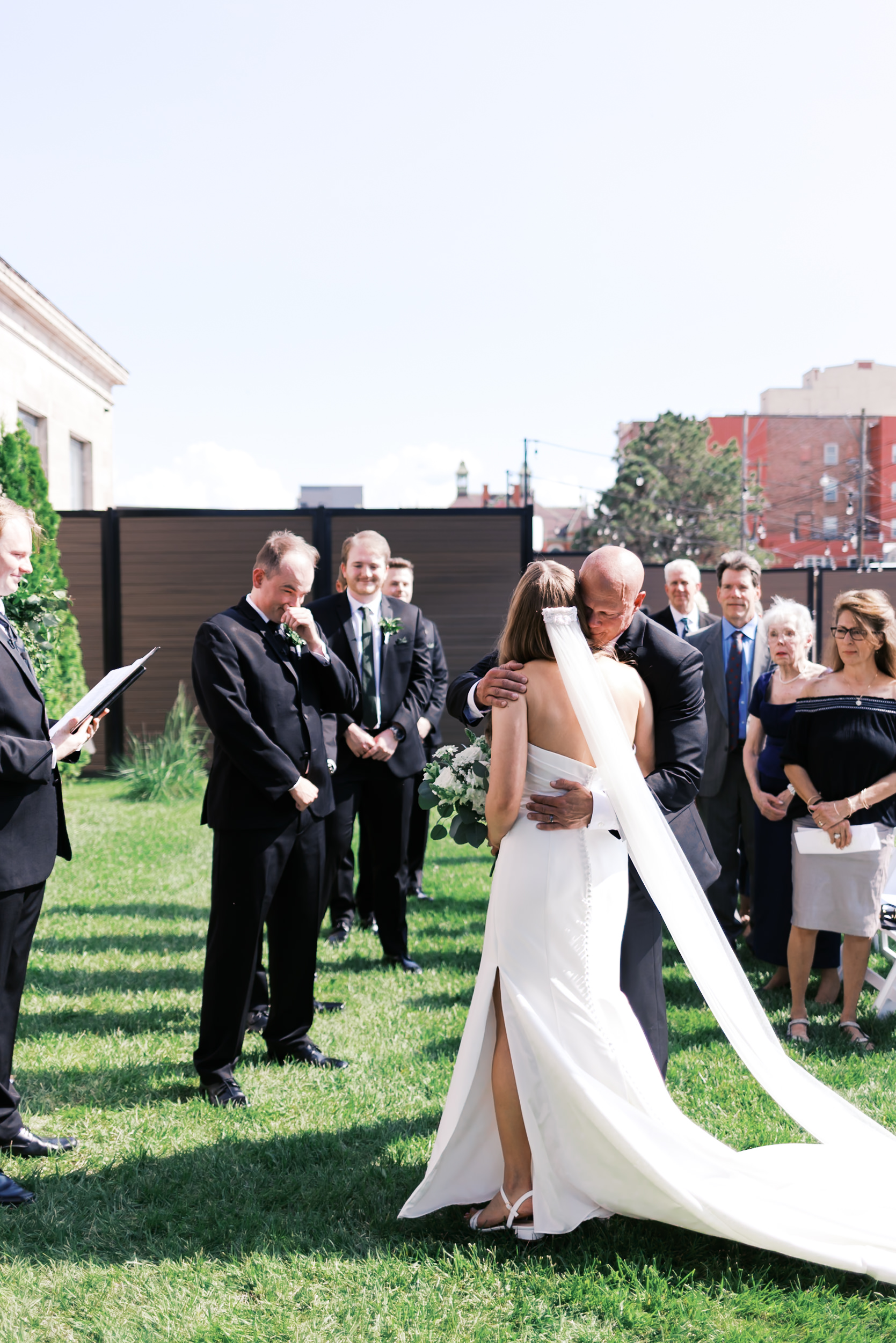 Bride hugging father as groom looks on tearfully