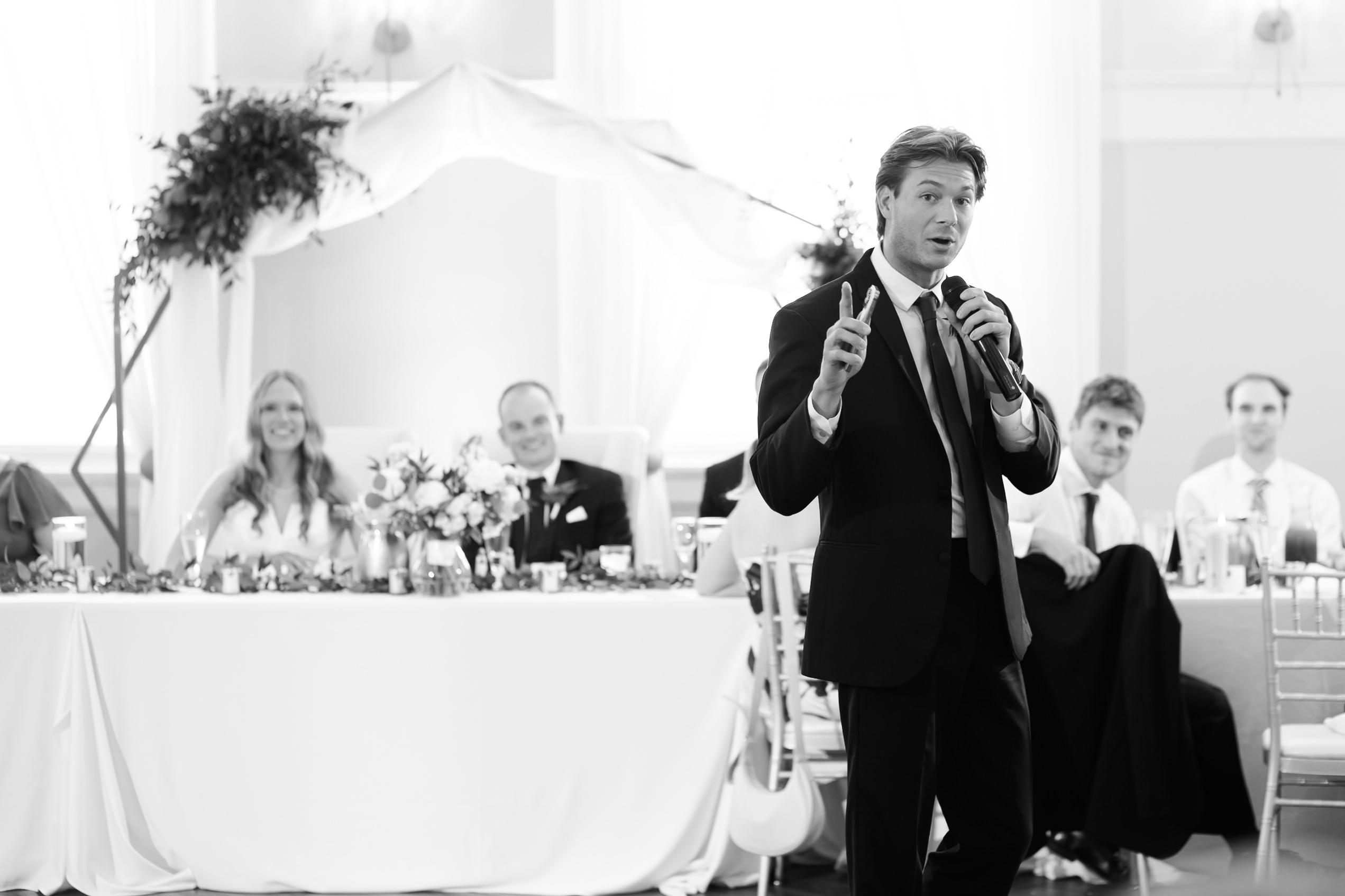 man giving a toast while bride and groom look on with smiles