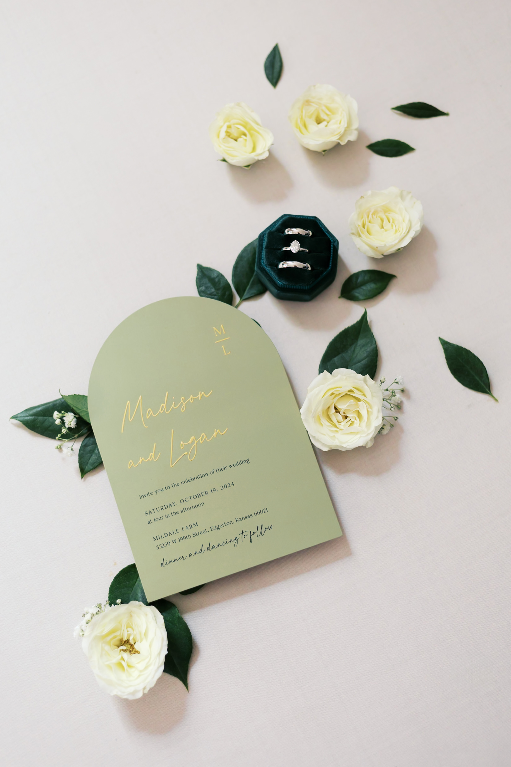 flatlay of green invitation and velvet green ringbox surrounded by greenery and white florals