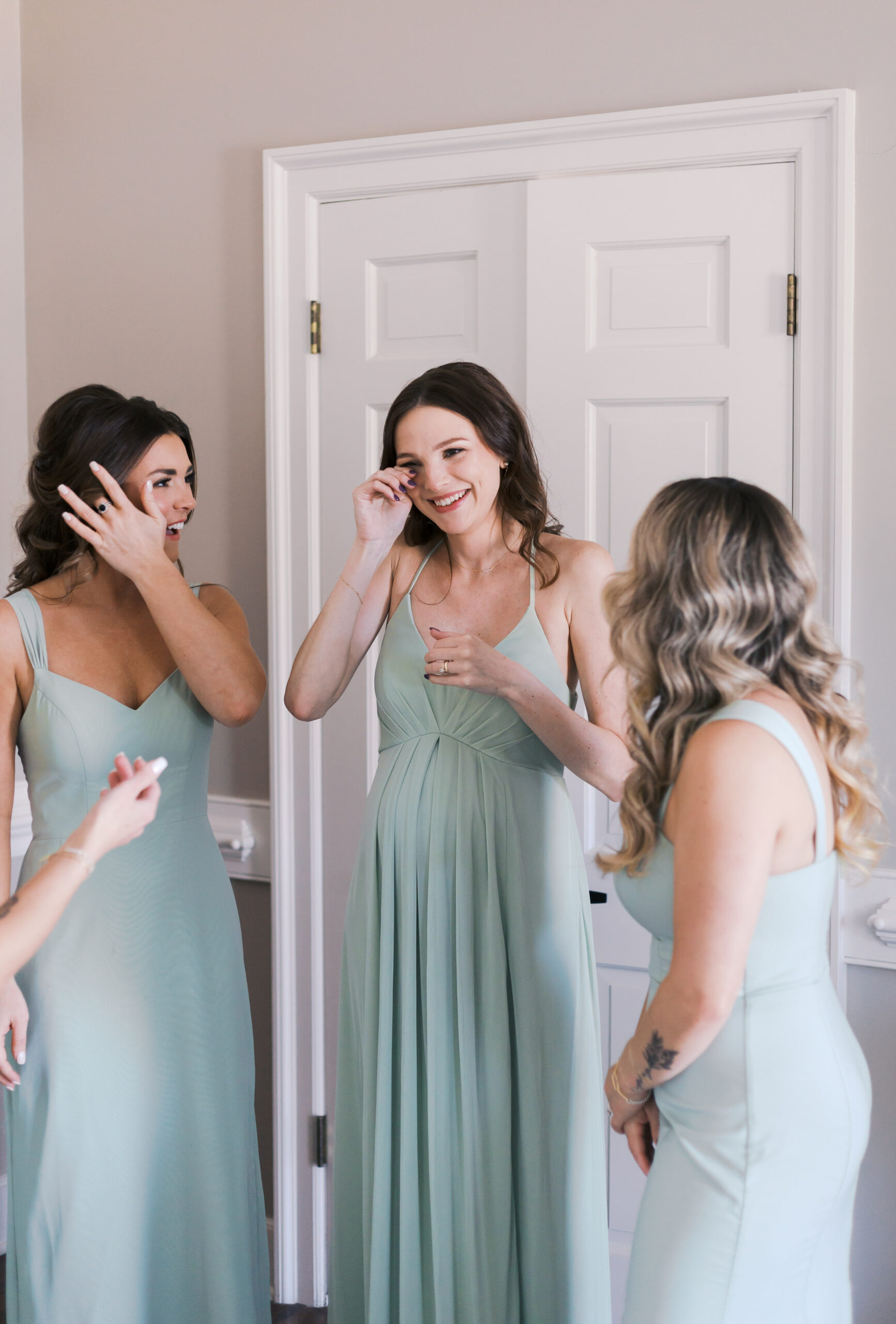 Bridesmaids in sage green dresses wiping away happy tears during a sweet pre-ceremony moment indoors.