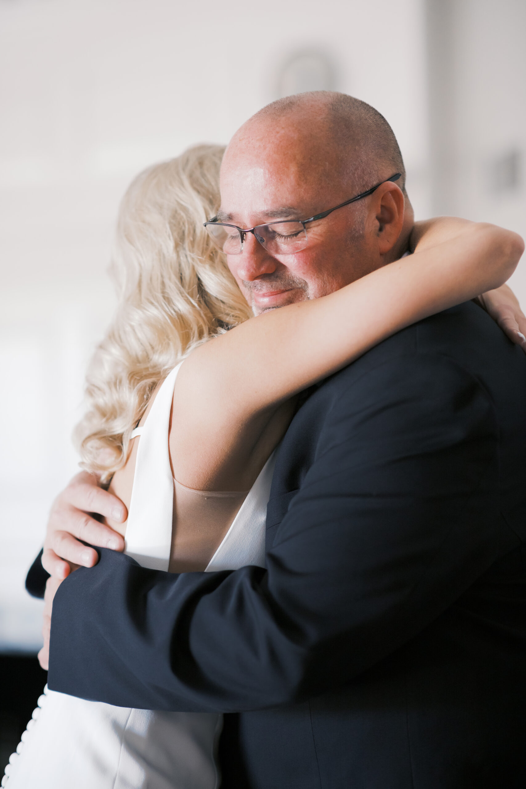 Close-up of father embracing the bride in her white gown, capturing a touching moment before the ceremony.