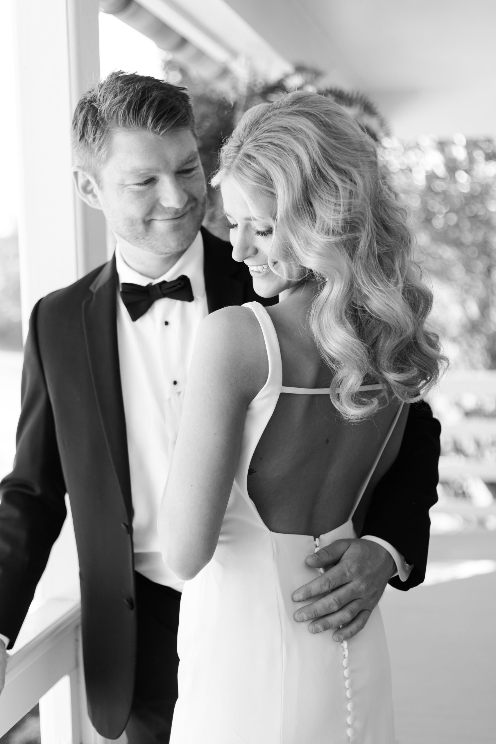 Close-up black and white photo of the groom smiling at the bride as she looks down with a soft smile on a farmhouse porch.