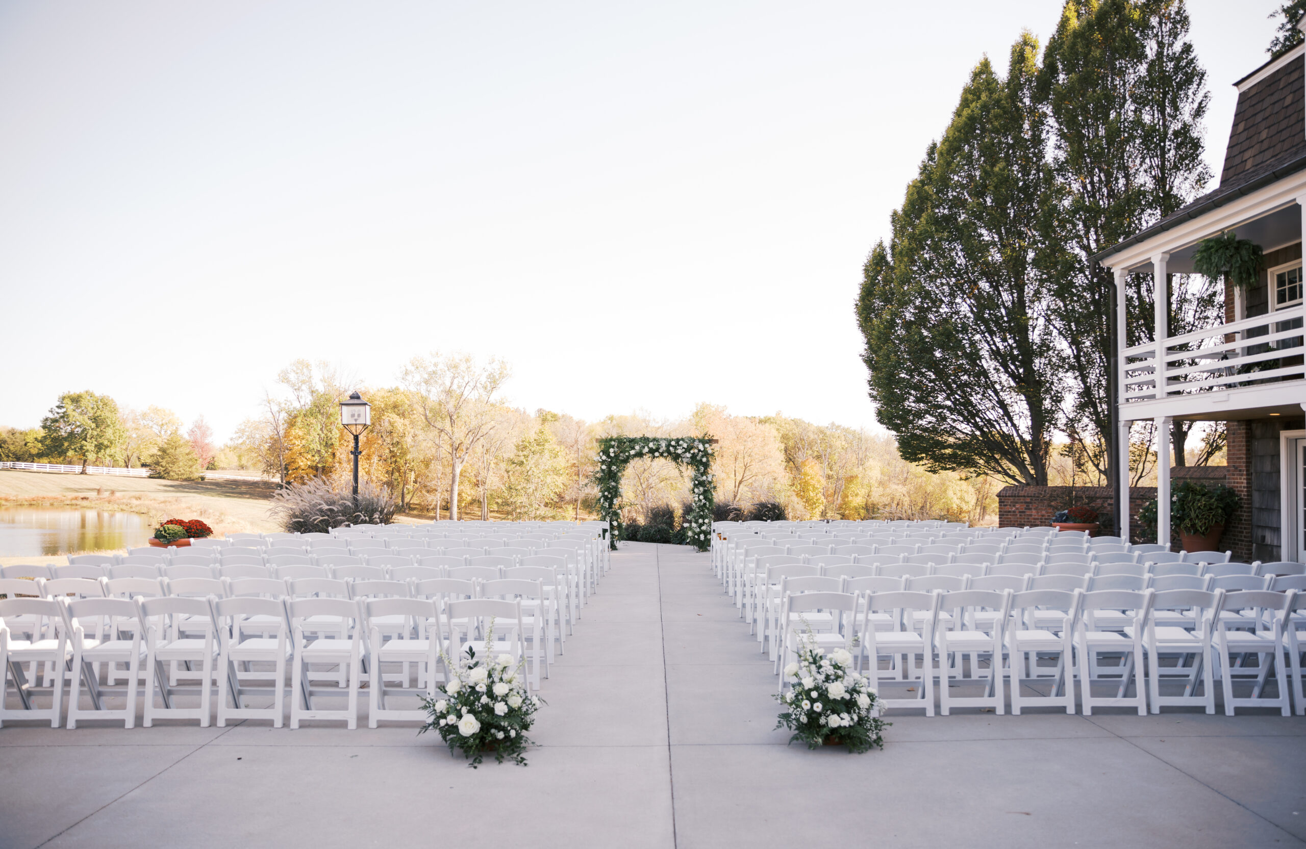 Elegant outdoor ceremony space at Mildale Farm with rows of white chairs and a floral arch, set against fall trees and a pond