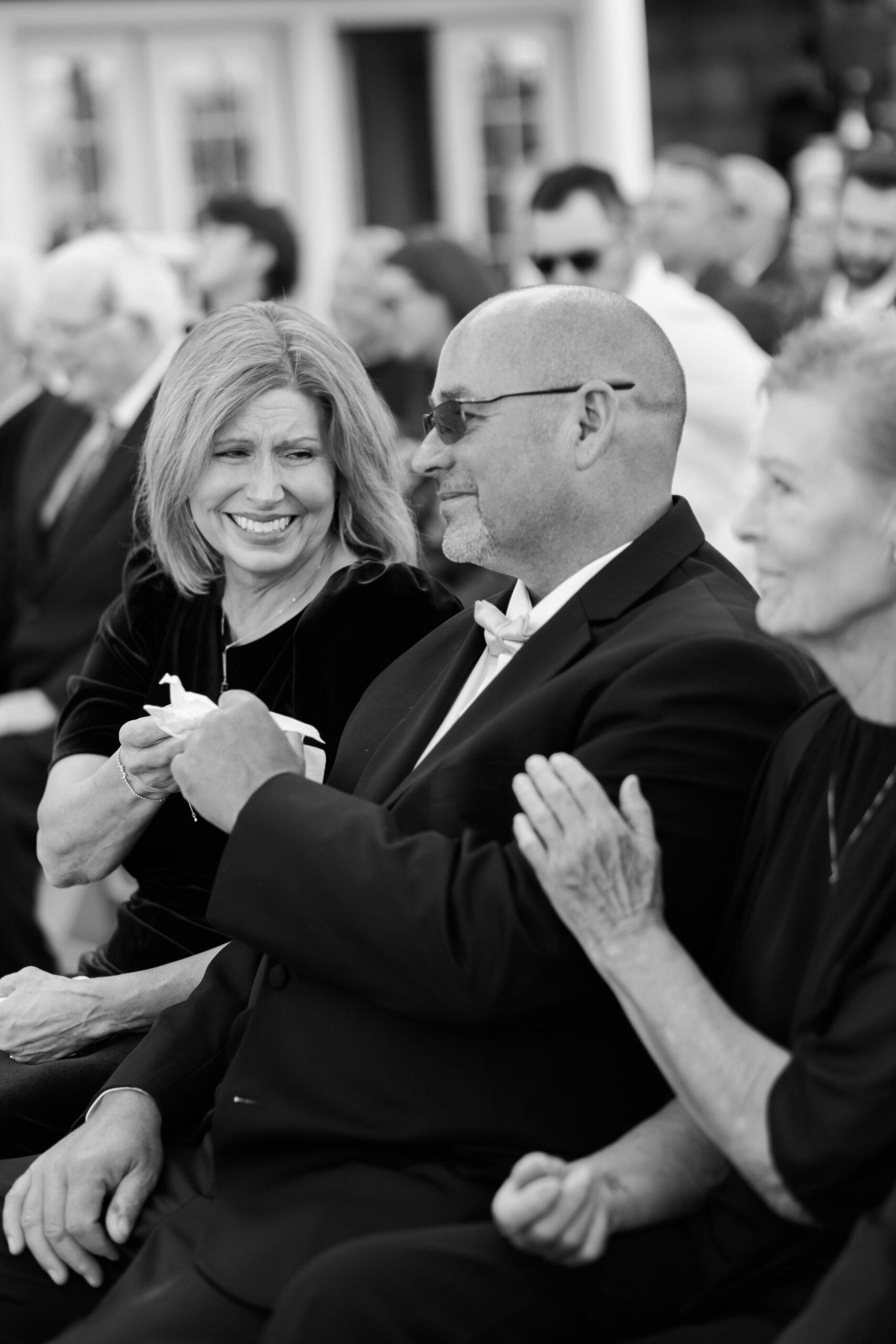 Black and white photo of seated parents smiling and holding hands during a touching moment at the wedding ceremony.