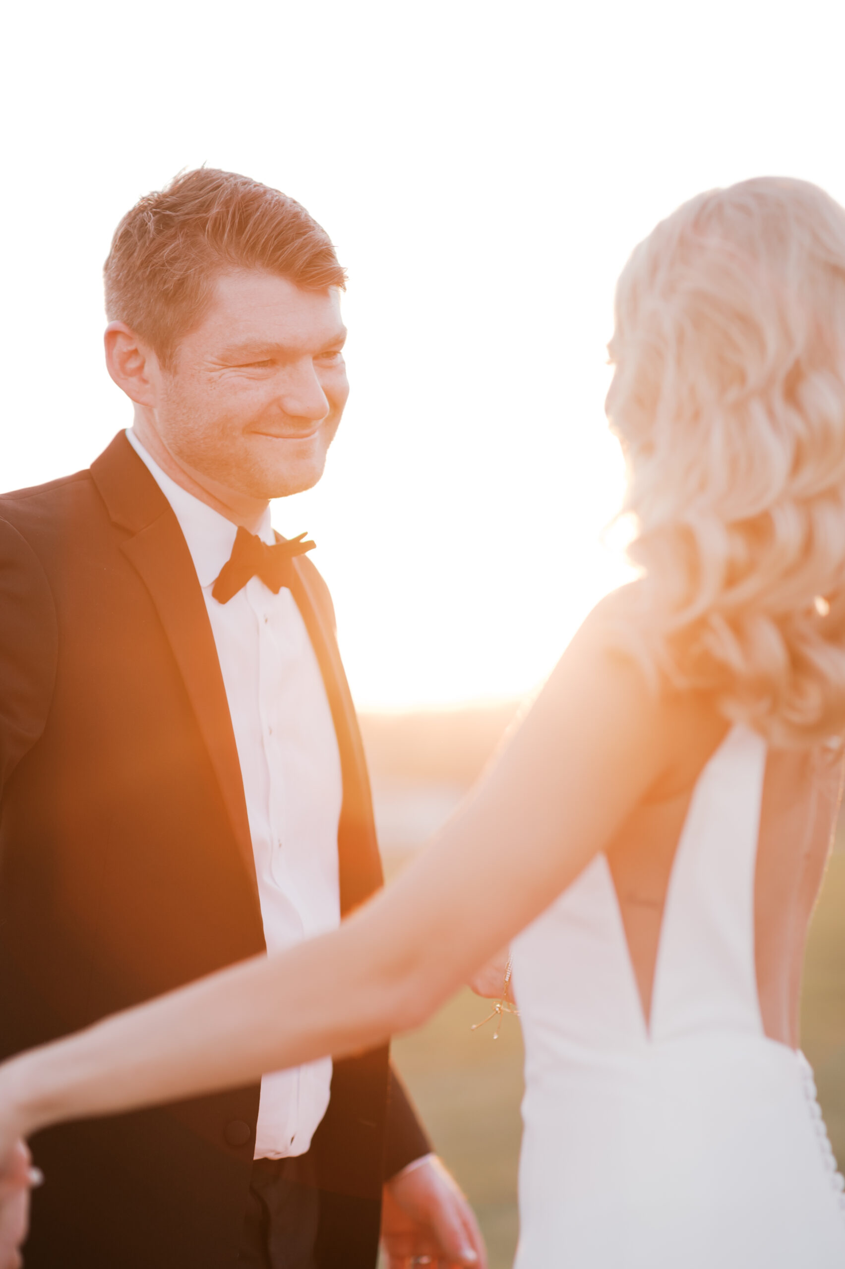Groom smiles at the bride as the sun sets behind them, casting a warm golden glow across the scene.