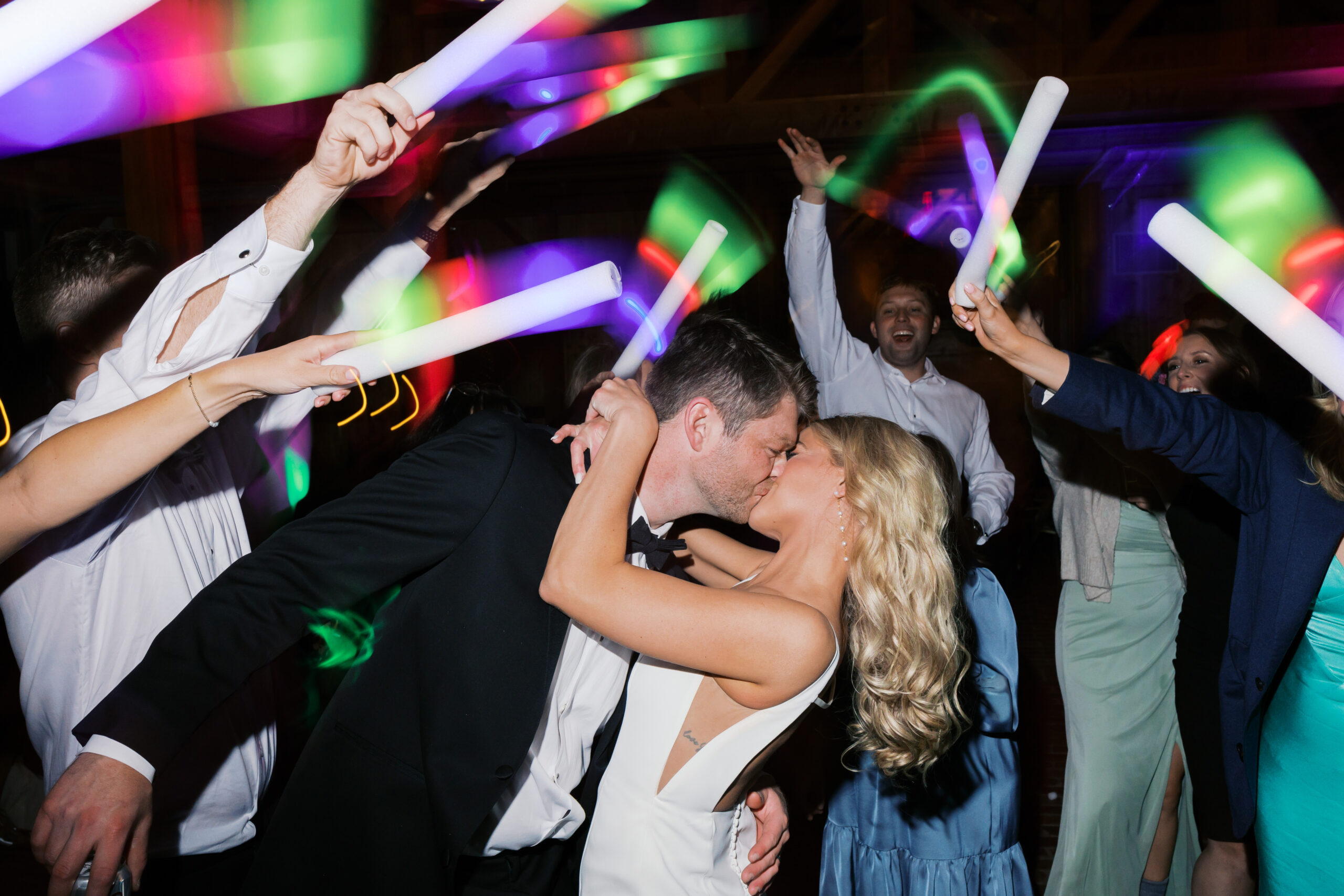 Bride and groom kissing on the dance floor surrounded by guests waving large glow sticks