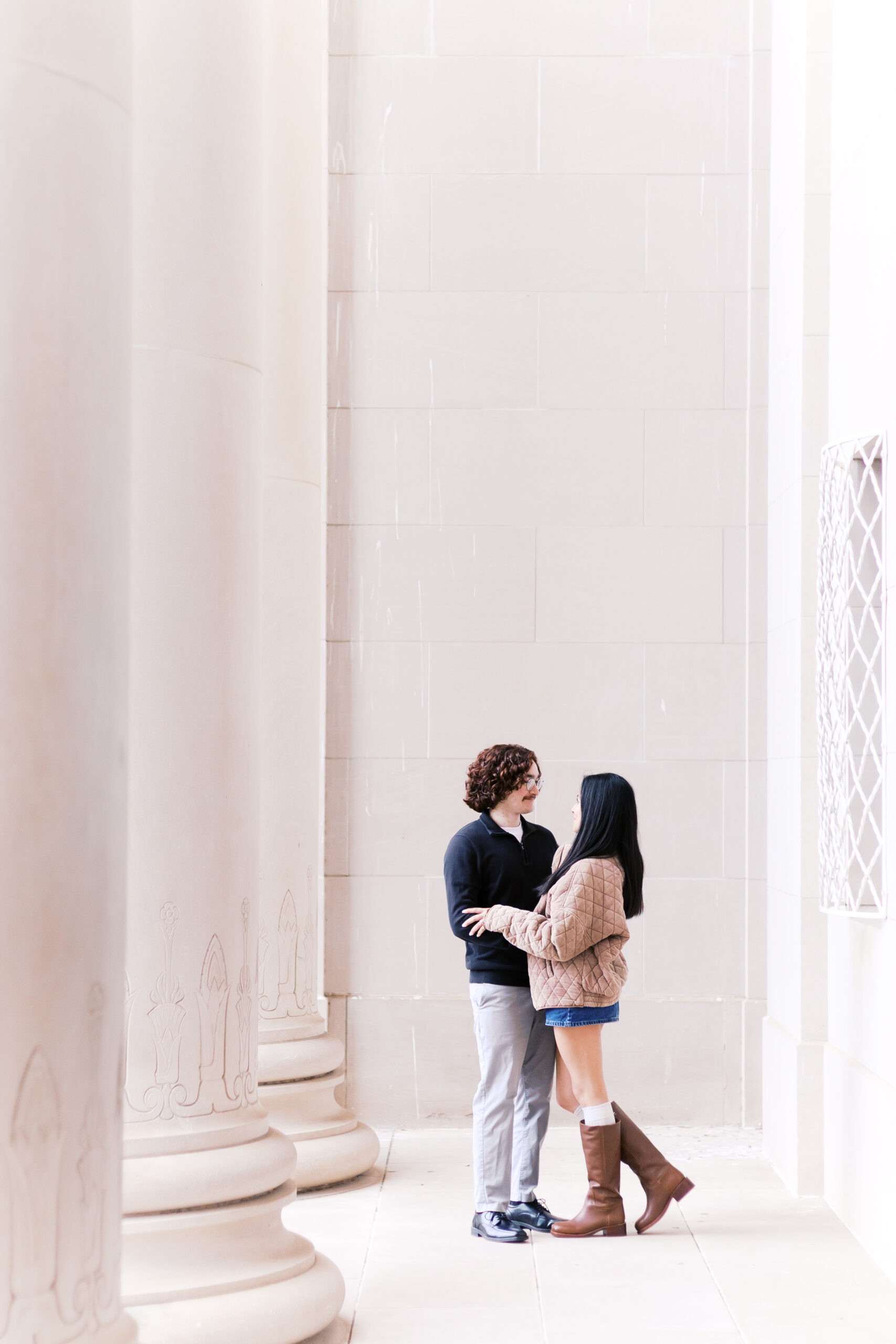 Couple standing close between tall stone columns at the Nelson-Atkins Museum, gazing at each other after their engagement.