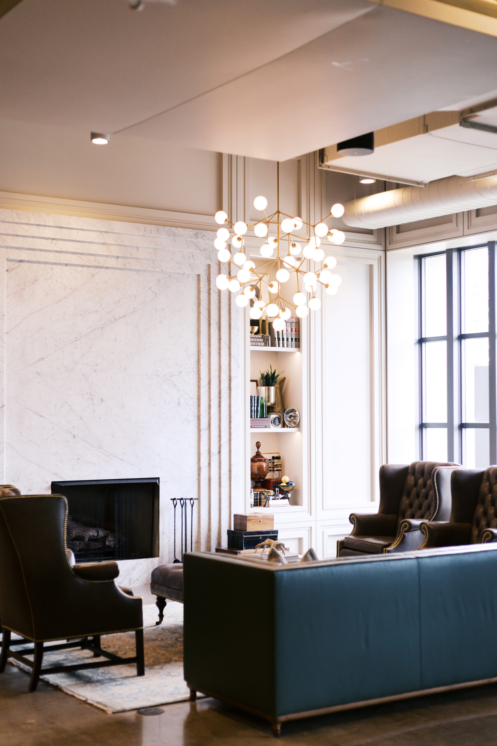 Elegant lounge at The Old Post Office Chicago with modern chandelier, tufted leather chairs, and marble fireplace.