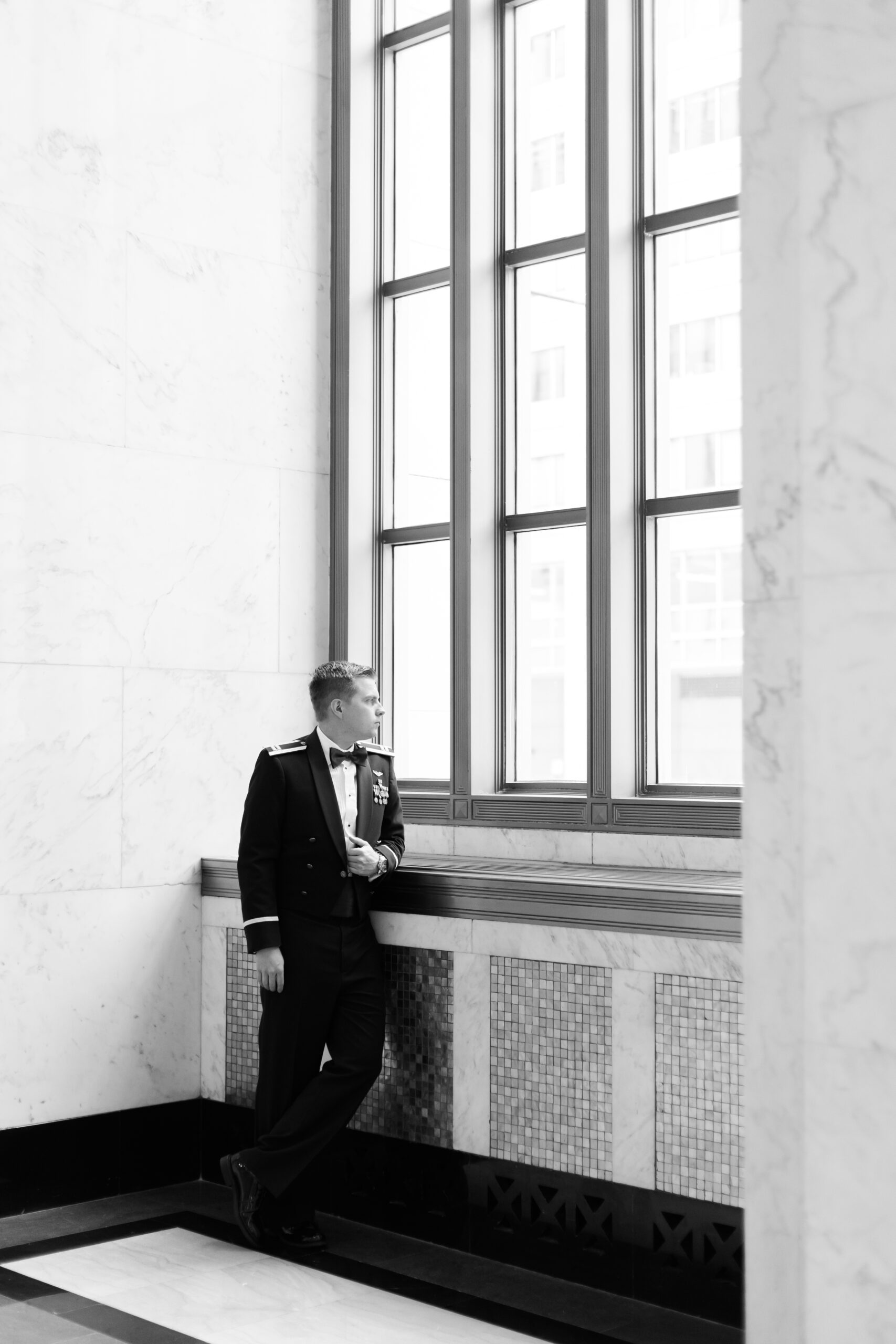 Black and white portrait of groom in military dress uniform looking out a tall window at The Old Post Office in Chicago.