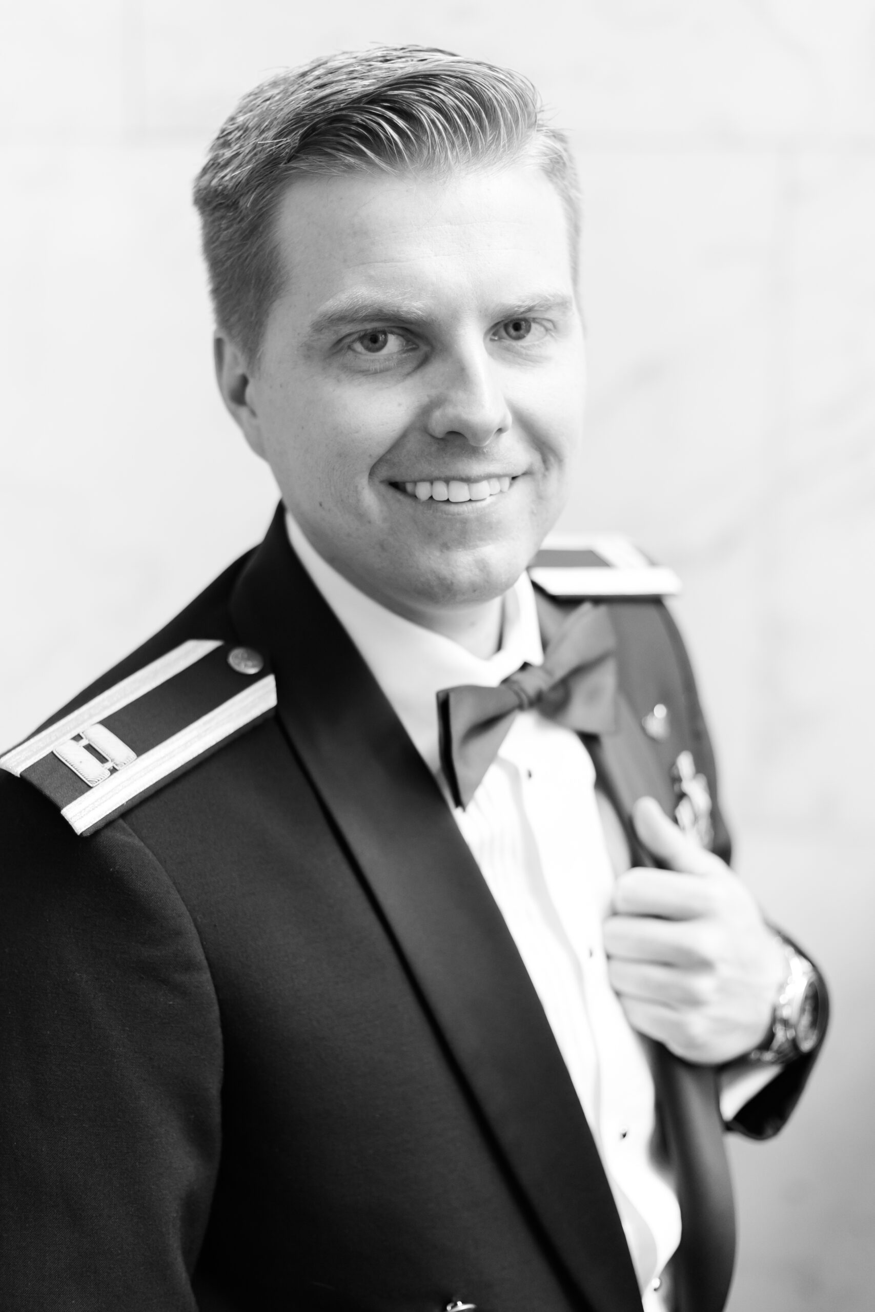 Black and white close-up of groom smiling in formal military dress uniform before the wedding ceremony.