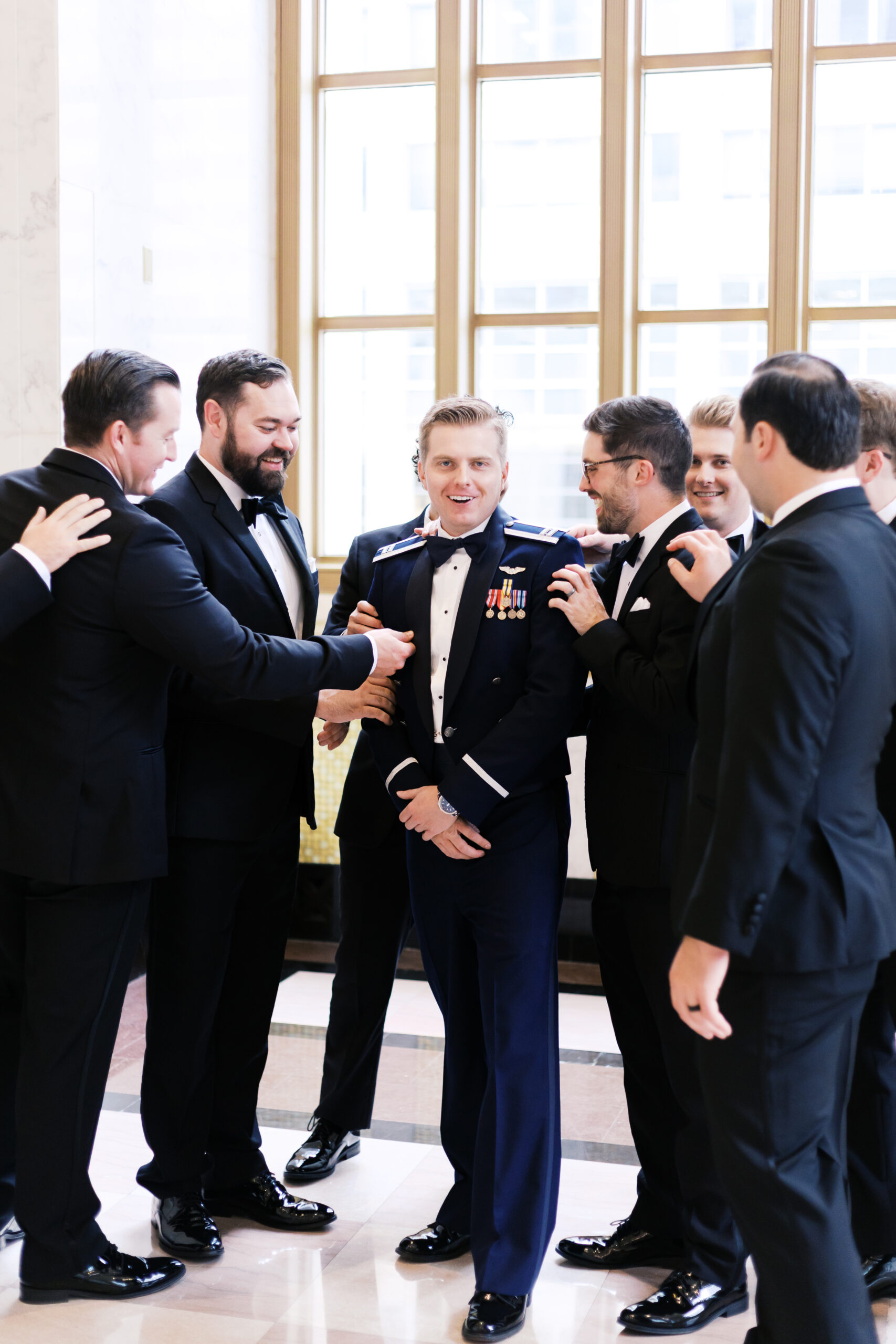 Groom in military dress uniform surrounded by groomsmen in tuxedos, getting ready at The Old Post Office Chicago