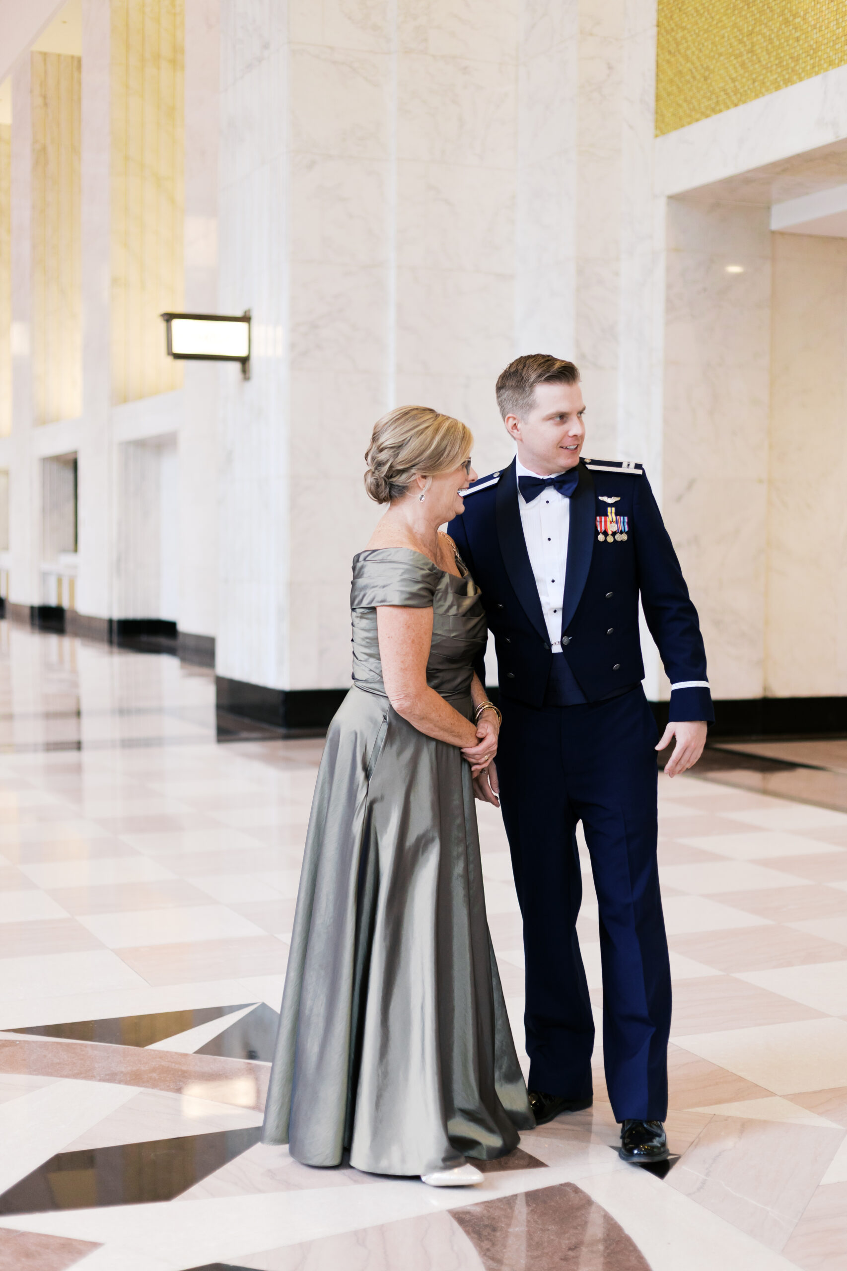 Groom in military dress uniform standing with his mother in a silver gown