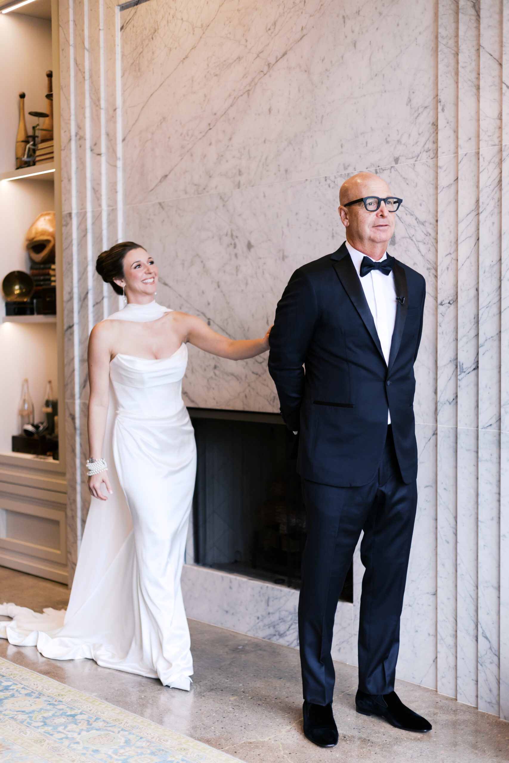 Bride in a white gown touching her father’s shoulder for their first look in an elegant marble room at The Old Post Office