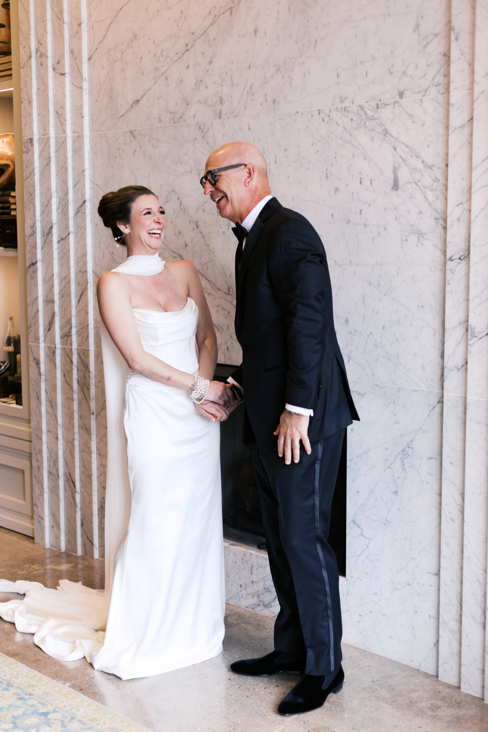 Bride in satin gown laughing with her father during a joyful moment before the ceremony.