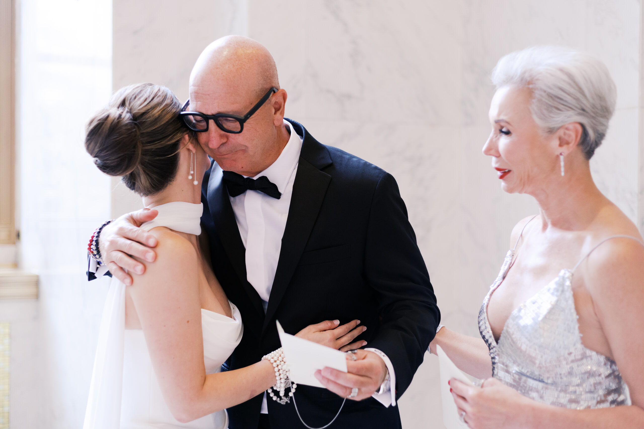 Bride hugging her father with emotion as her mother stands nearby during a family moment before the wedding.