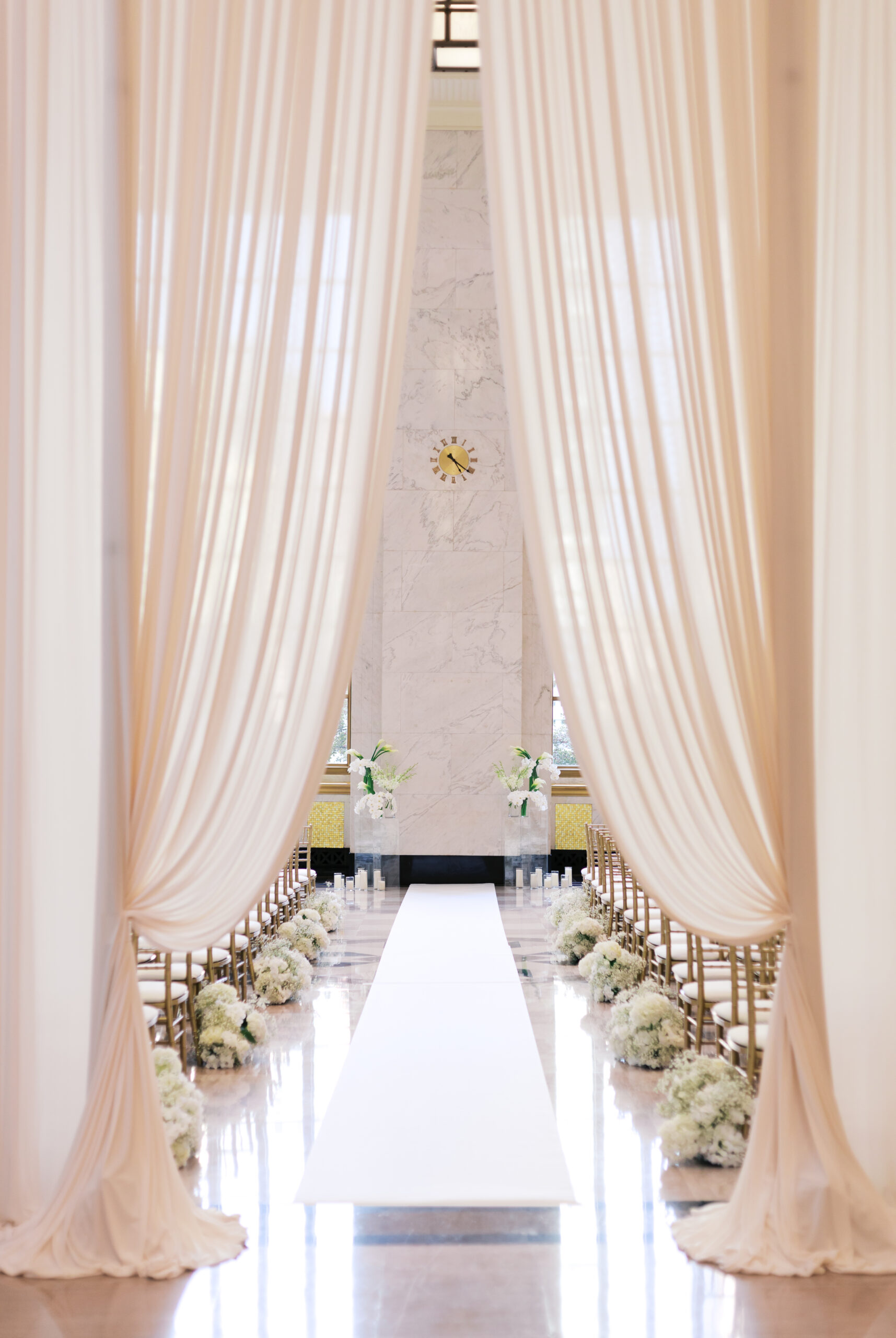 Elegant indoor ceremony setup with blush drapes, white aisle runner, gold chairs, and floral arrangements at The Old Post Office Chicago.