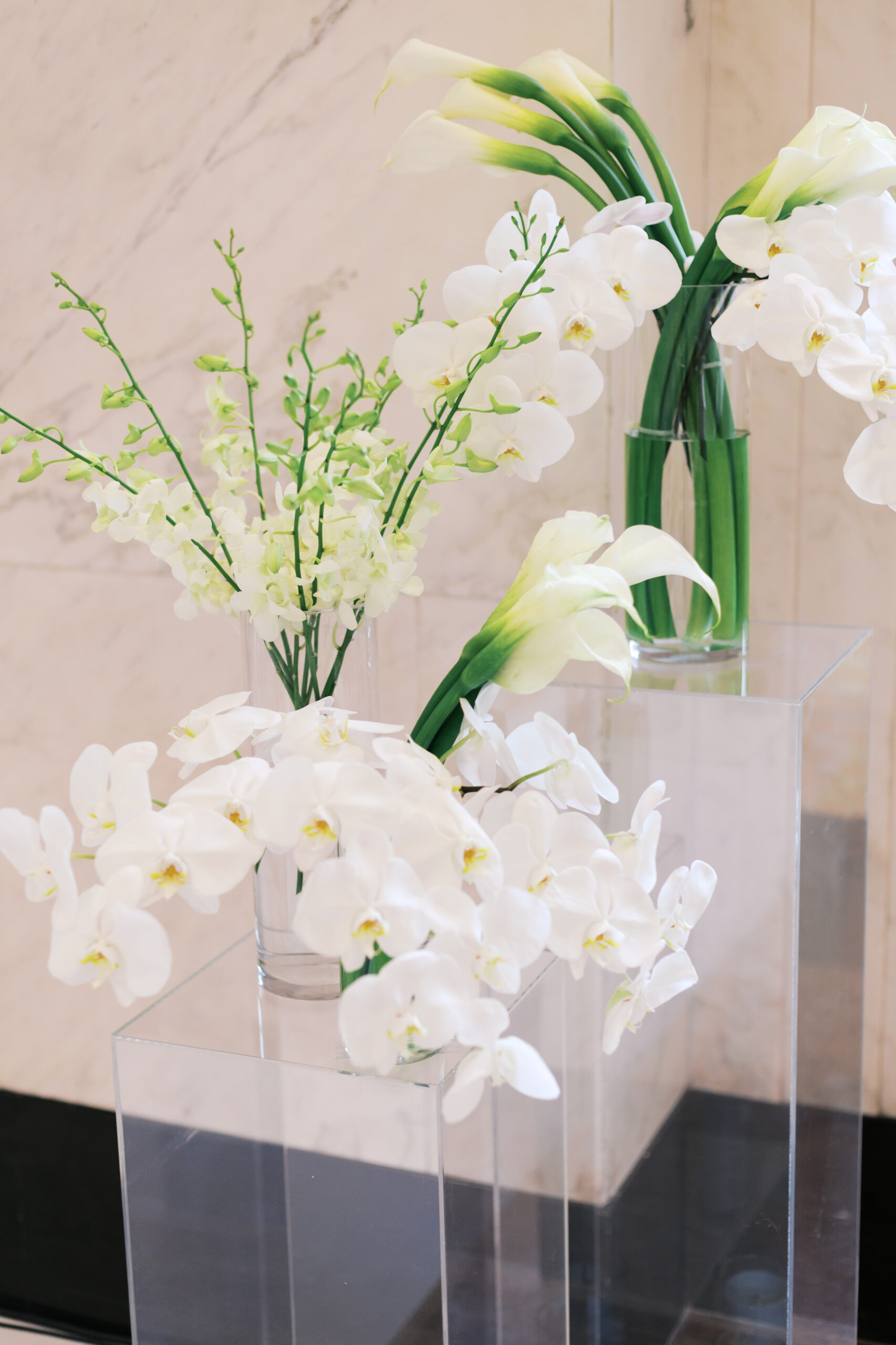 Close-up of modern white wedding florals with orchids, calla lilies, and snapdragons in tall glass vases.