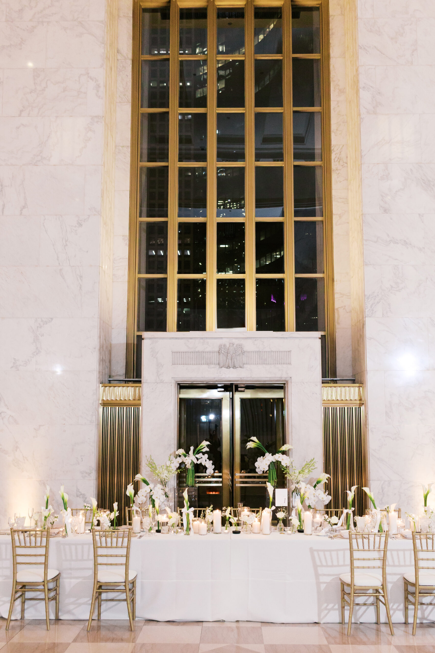 Reception table with white and green floral arrangements and candles in front of the tall windows at the Old Post Office Chicago