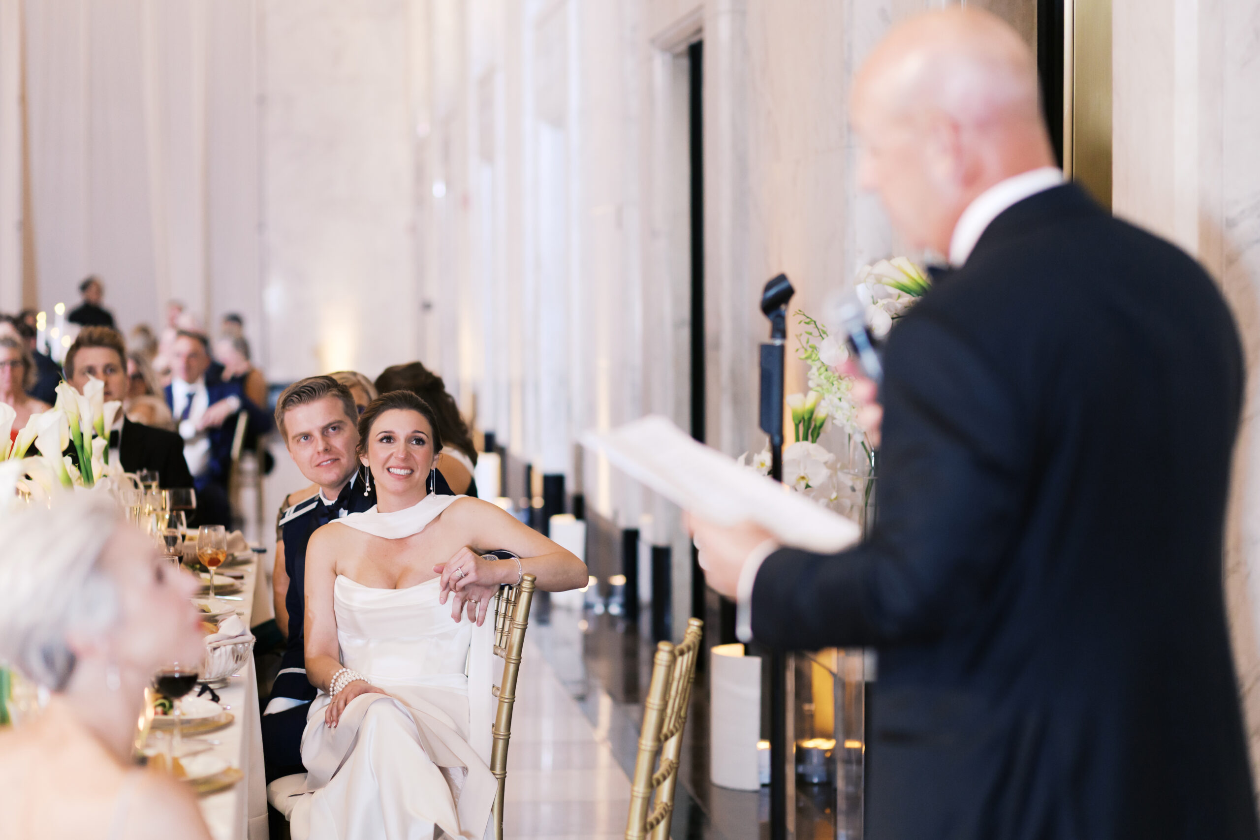 Father of the bride giving a toast as the newly married couple looks on and smiles.