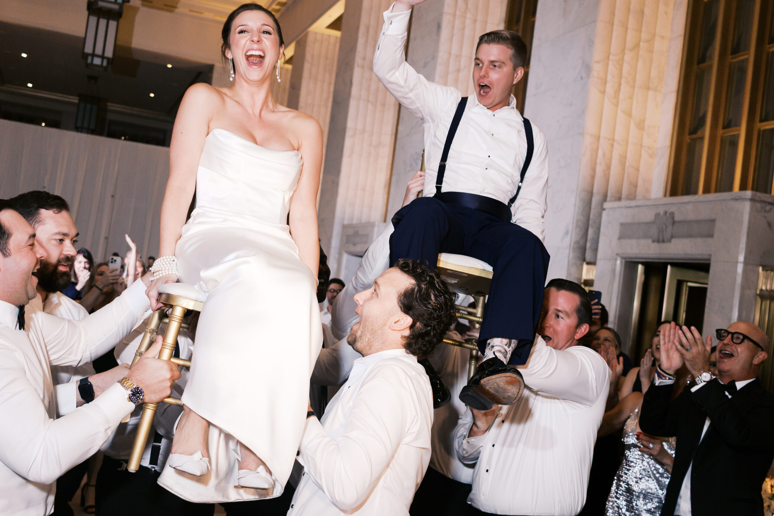 Bride and groom being lifted on chairs by men on the dance floor.