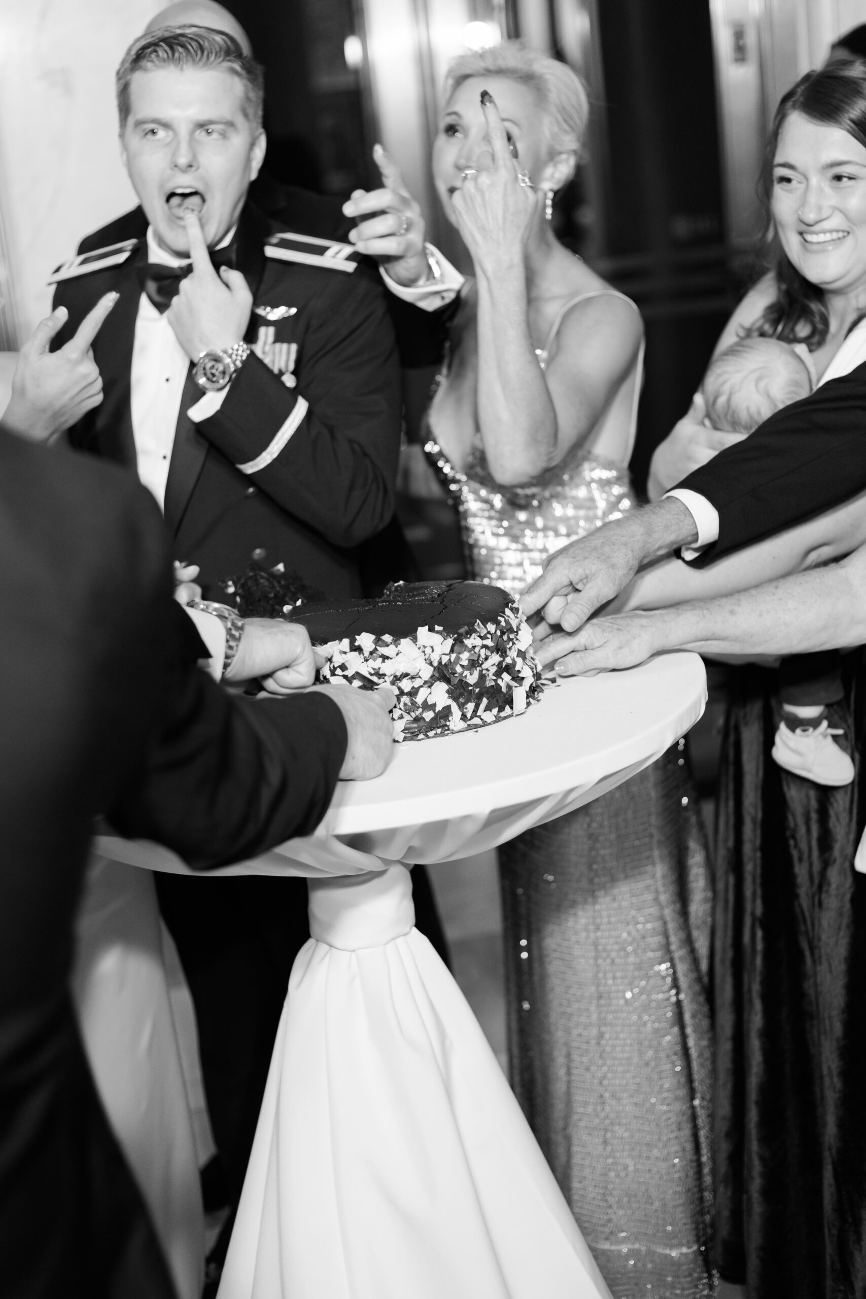 Groom and guests tasting the cake with their fingers in a black and white image.
