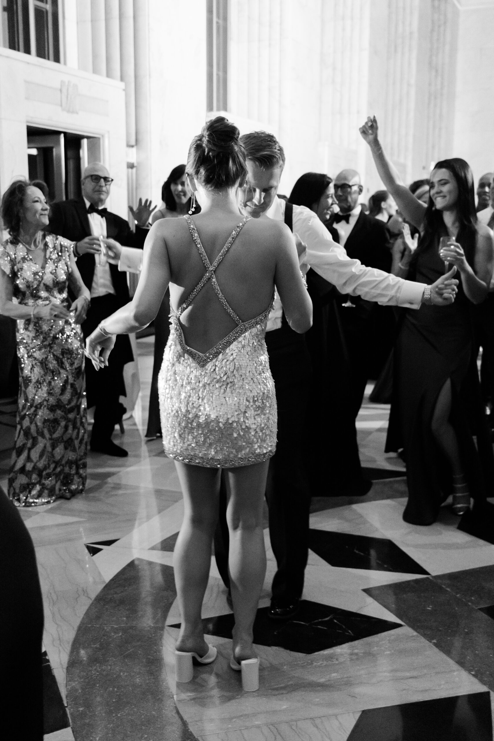 Black and white image of the bride and groom dancing surrounded by guests.