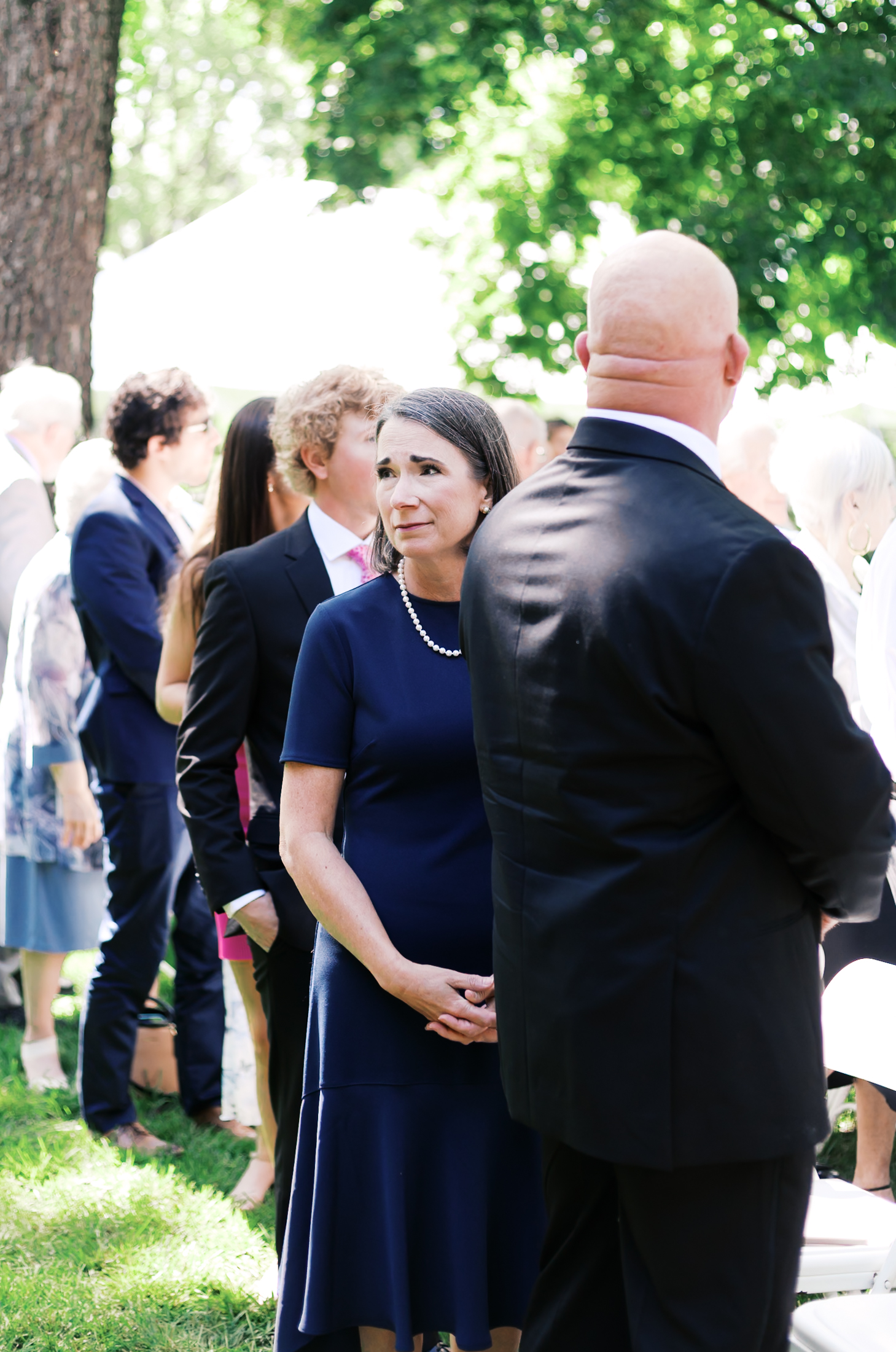 Close-up of woman in a navy floral dress holding tissues and a phone, visibly emotional during the ceremony.