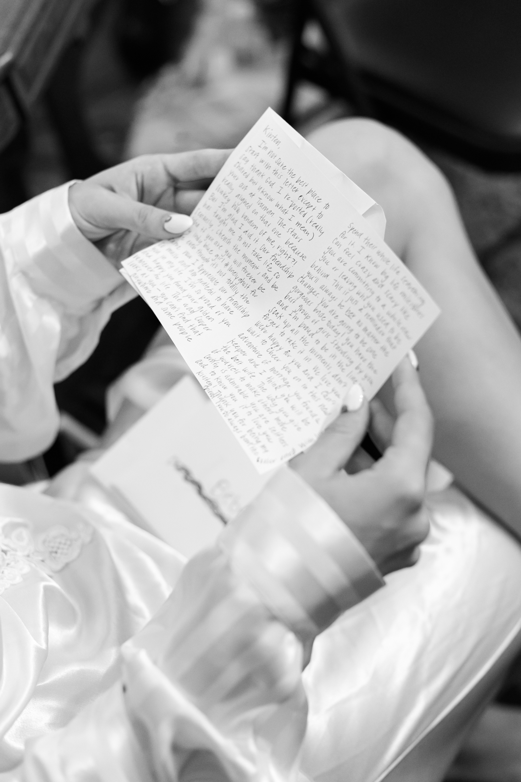 Close-up of a bride holding a handwritten letter while wearing a satin robe, captured in a quiet pre-ceremony moment.