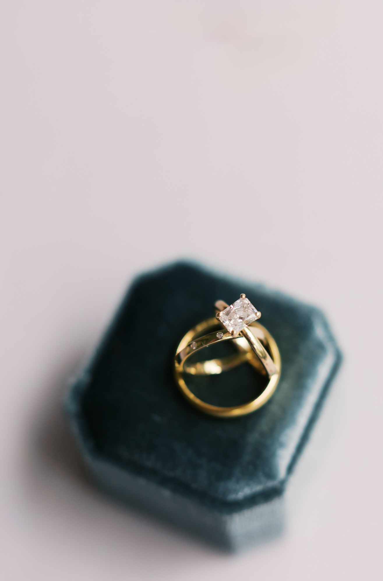Gold wedding bands and a solitaire engagement ring with a square diamond set in a teal velvet ring box.