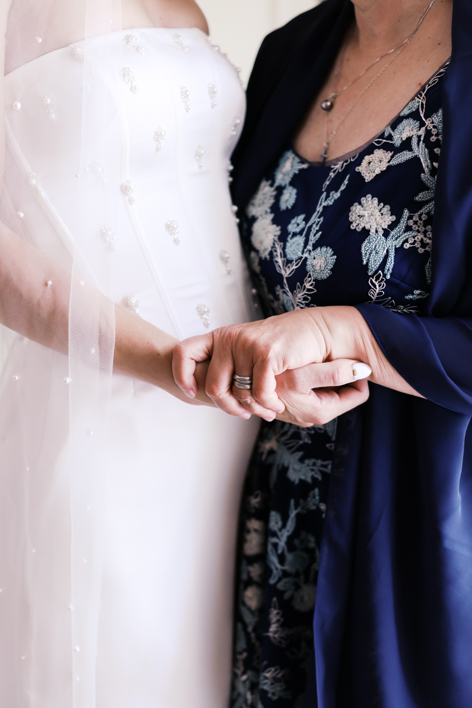 Detail shot of bride’s hand clasped with a woman in a navy floral dress, showing connection before the ceremony.
