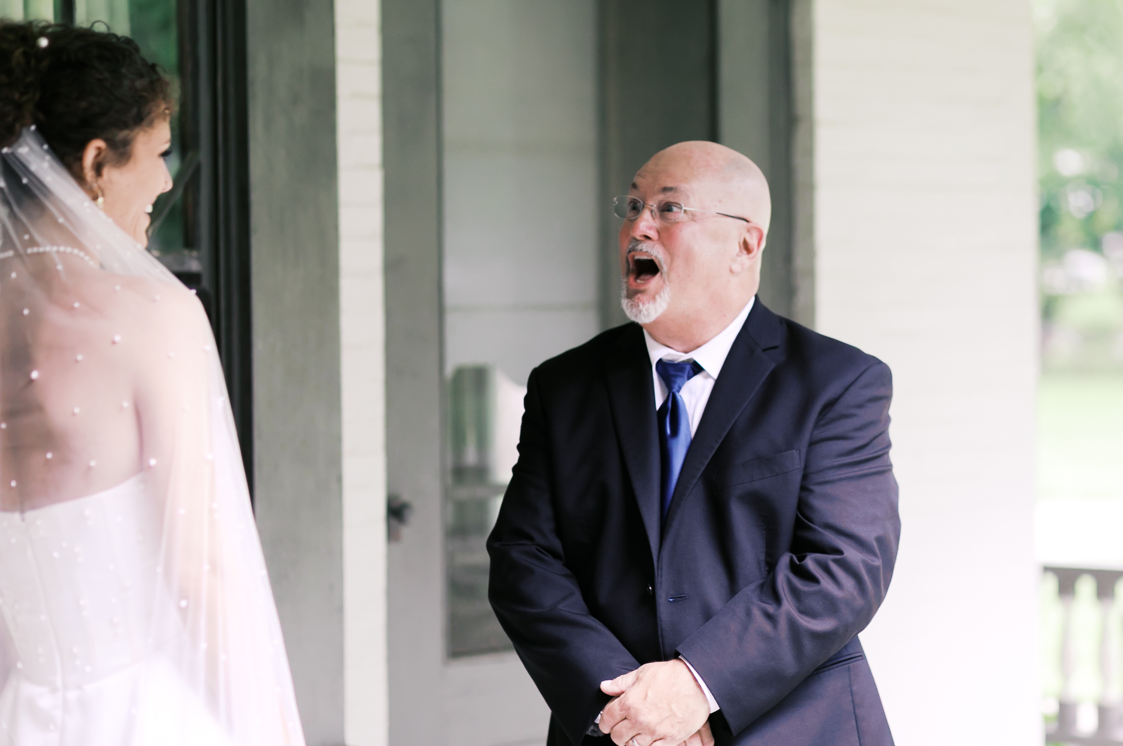 An older man reacts with surprise and emotion as he sees the bride in her wedding gown on a porch.