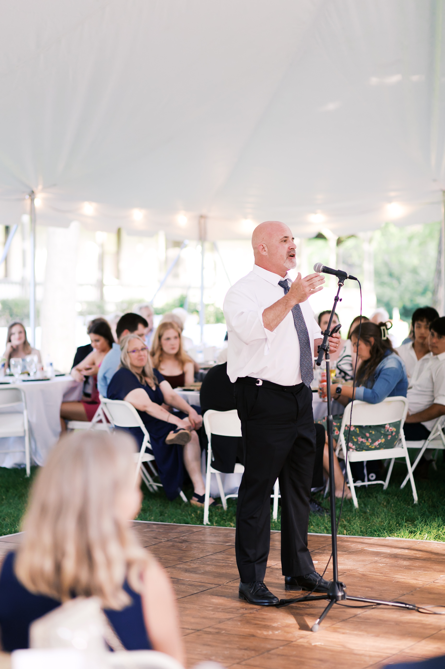 Man in a white shirt, black pants and gray tie giving a wedding speech.