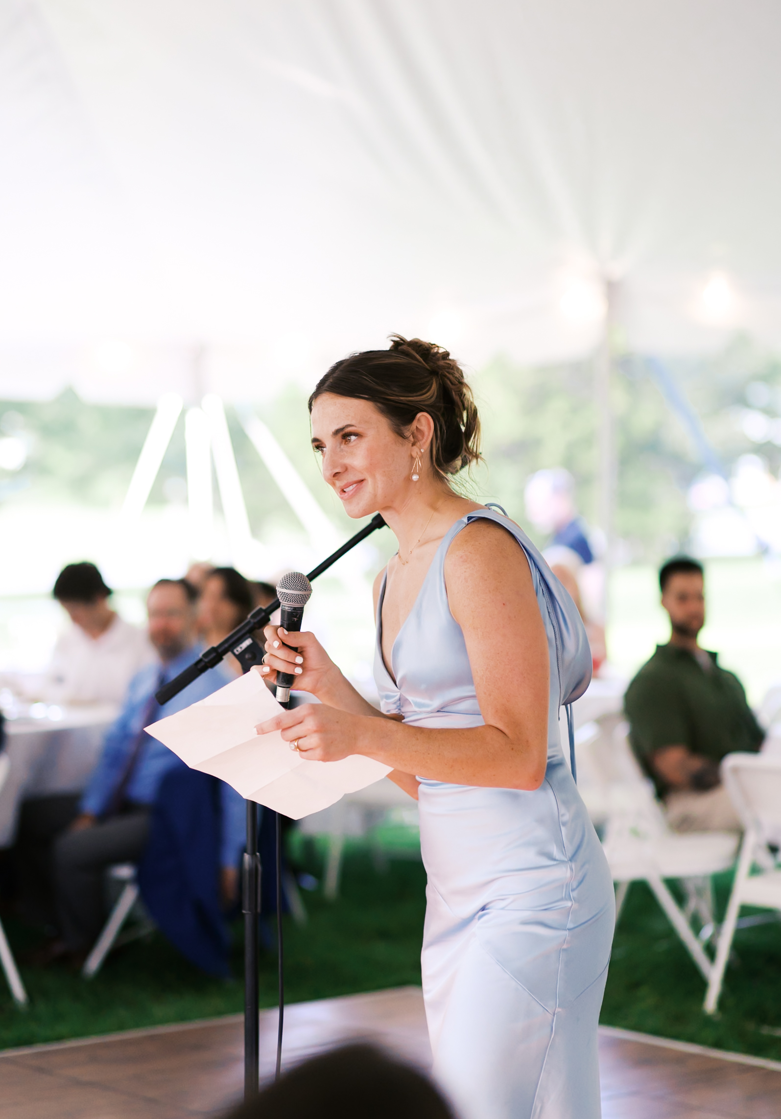 Woman in blue dress holding a microphone giving a toast.