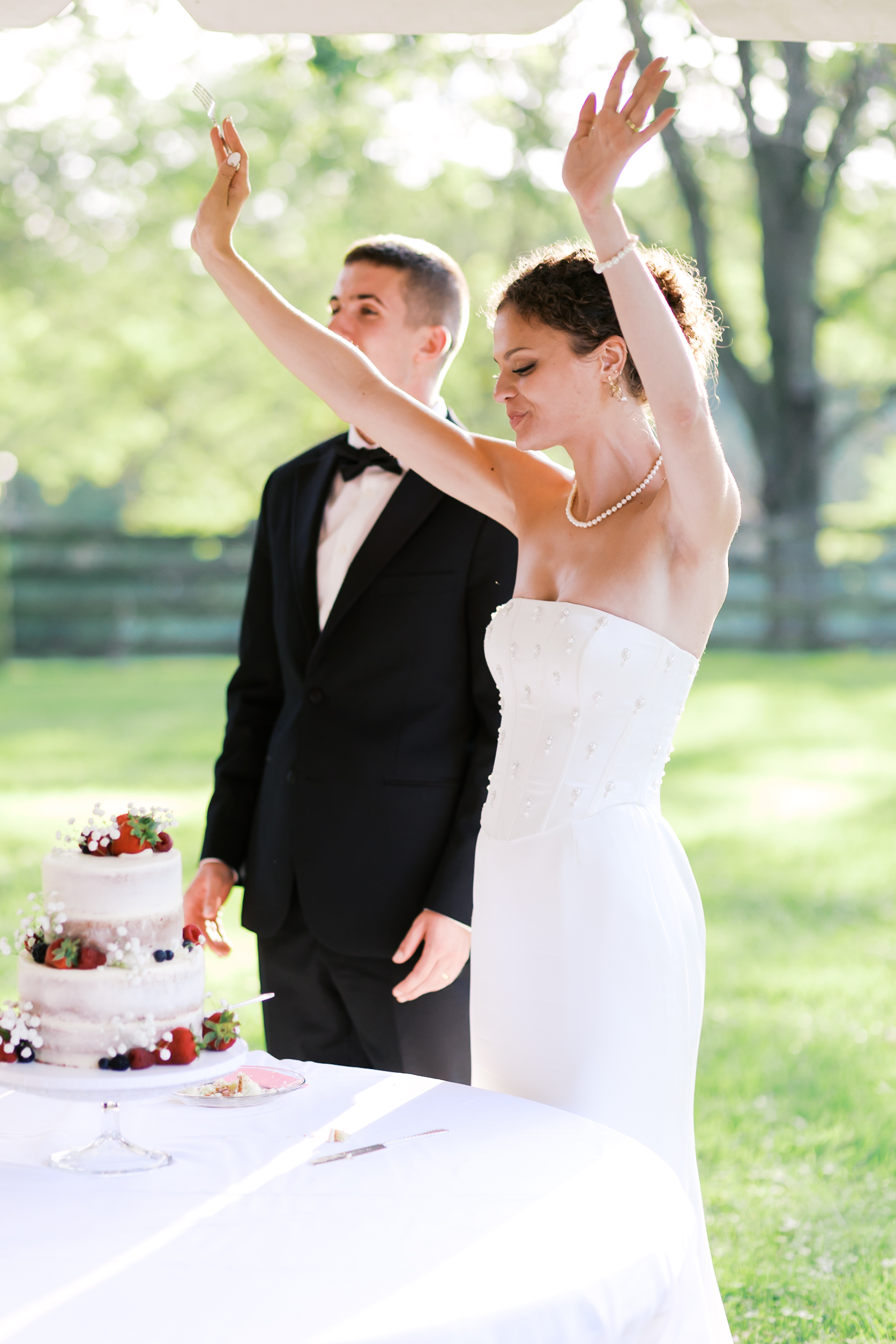 Bride raising her arms after cutting the cake.