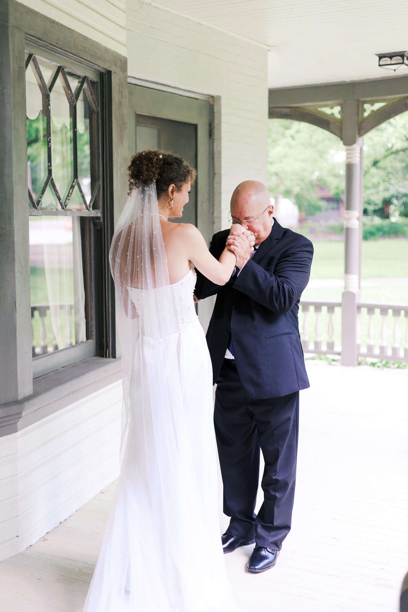 Black and white image of an older man in a suit gently kissing the bride’s hands in an intimate pre-ceremony moment.