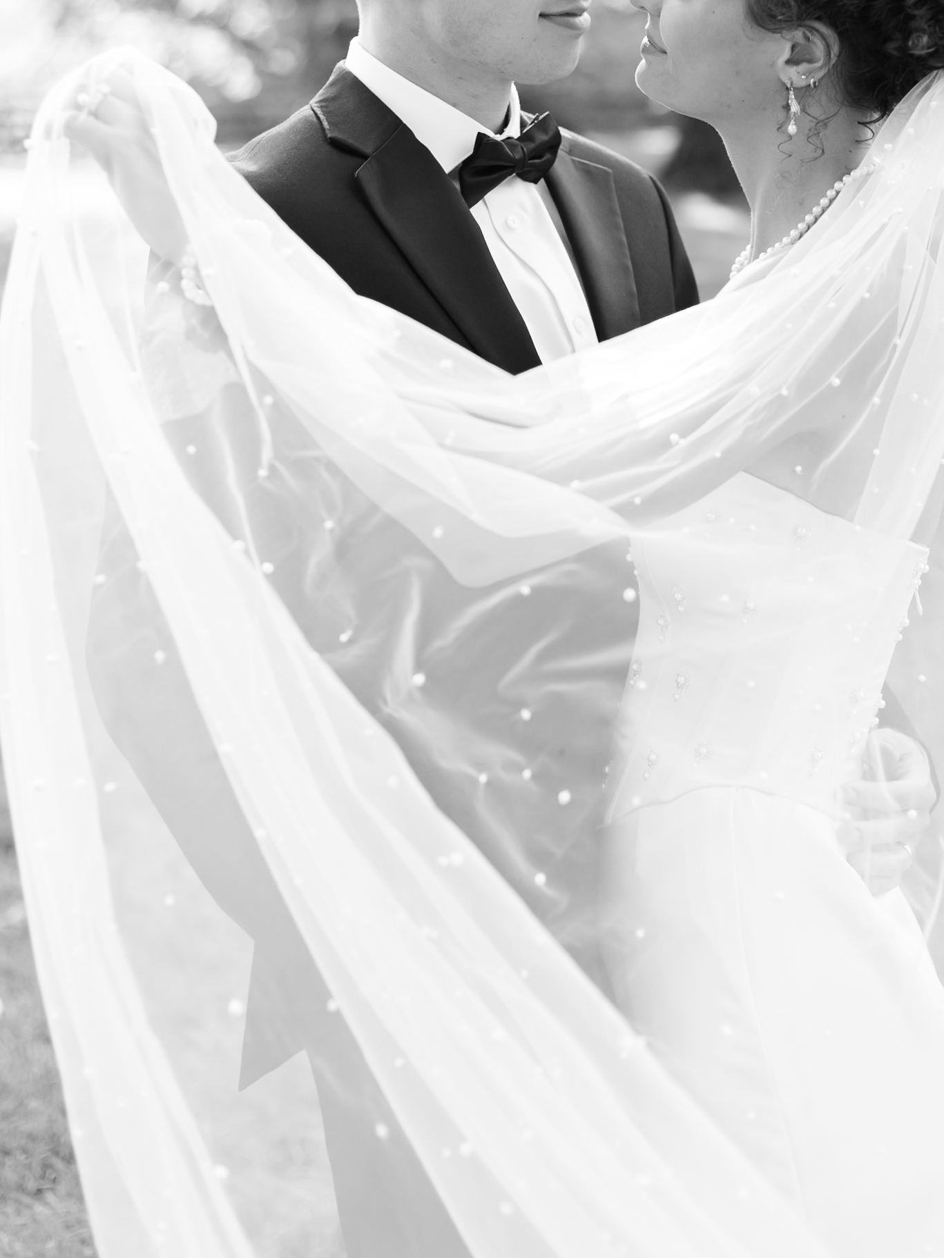 Intimate black and white portrait of the bride and groom gazing at each other beneath a sheer, pearl-dotted veil.
