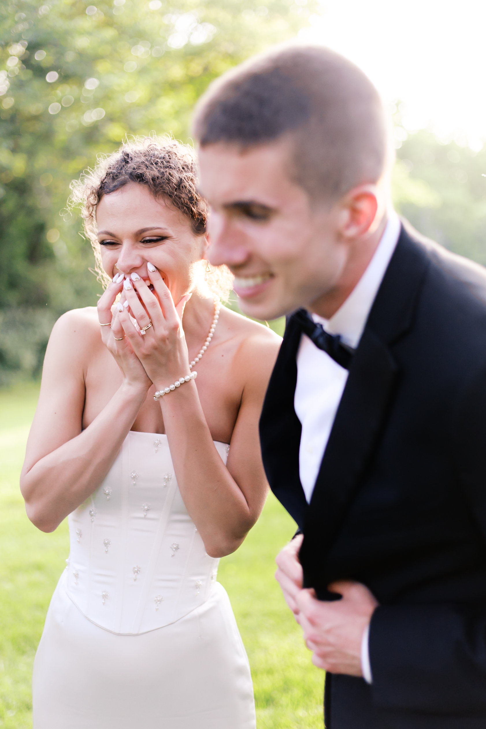 Bride covering her mouth as she laughs as groom leans in smiling in foreground.