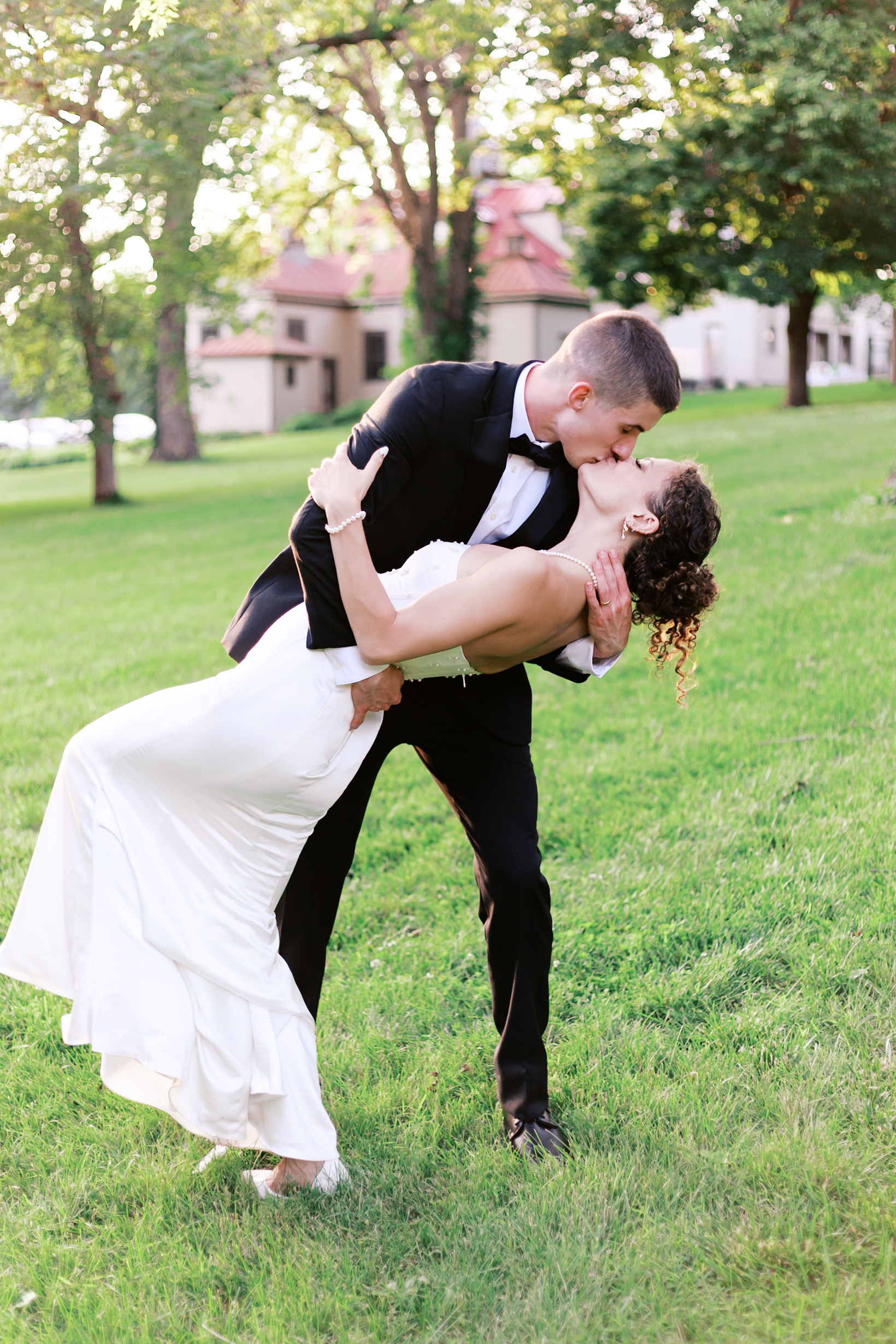 Groom dipping bride and kissing her on a lawn in front of a home.