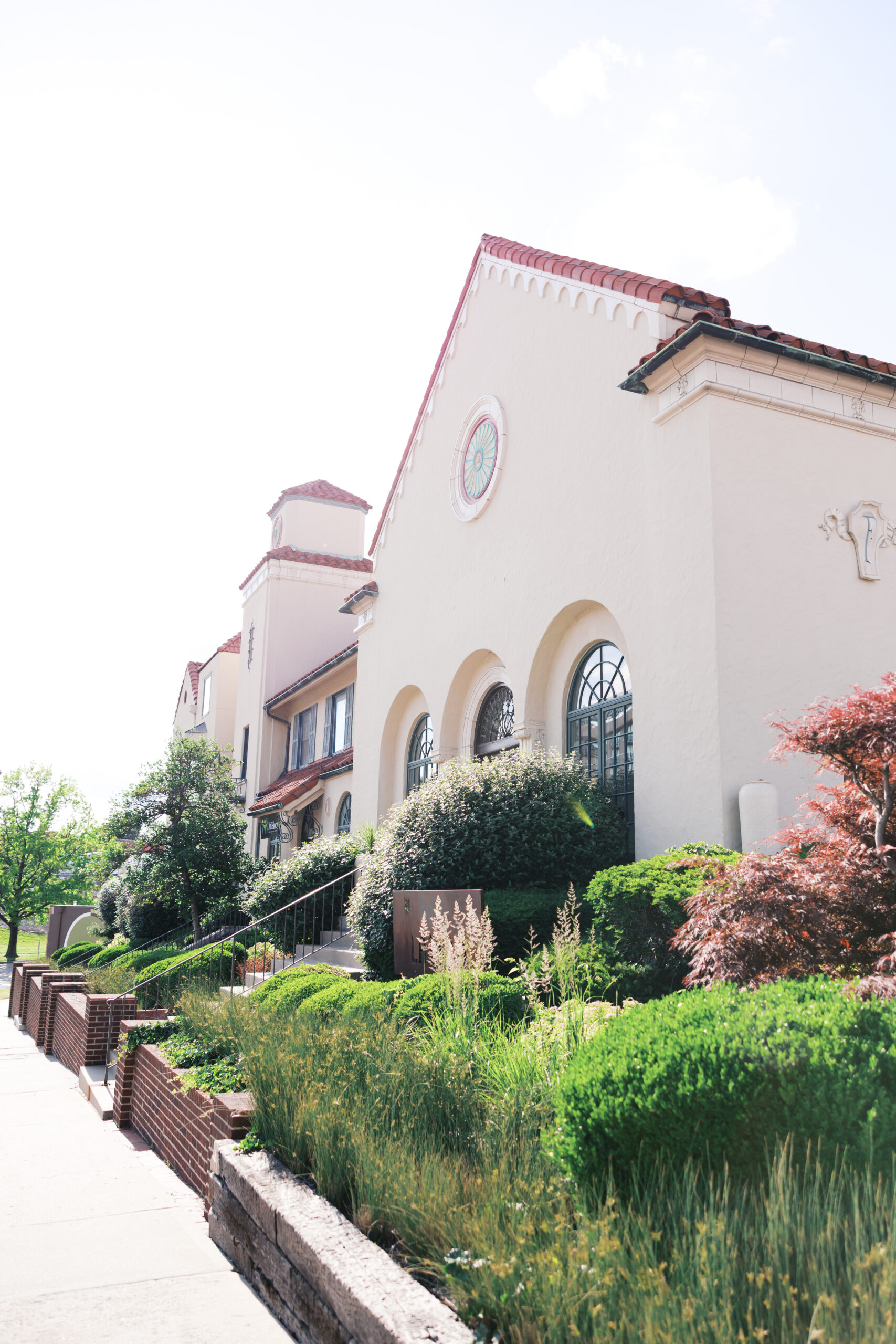 Spanish-style wedding venue with cream stucco walls, red tile roof, and manicured greenery along the sidewalk.