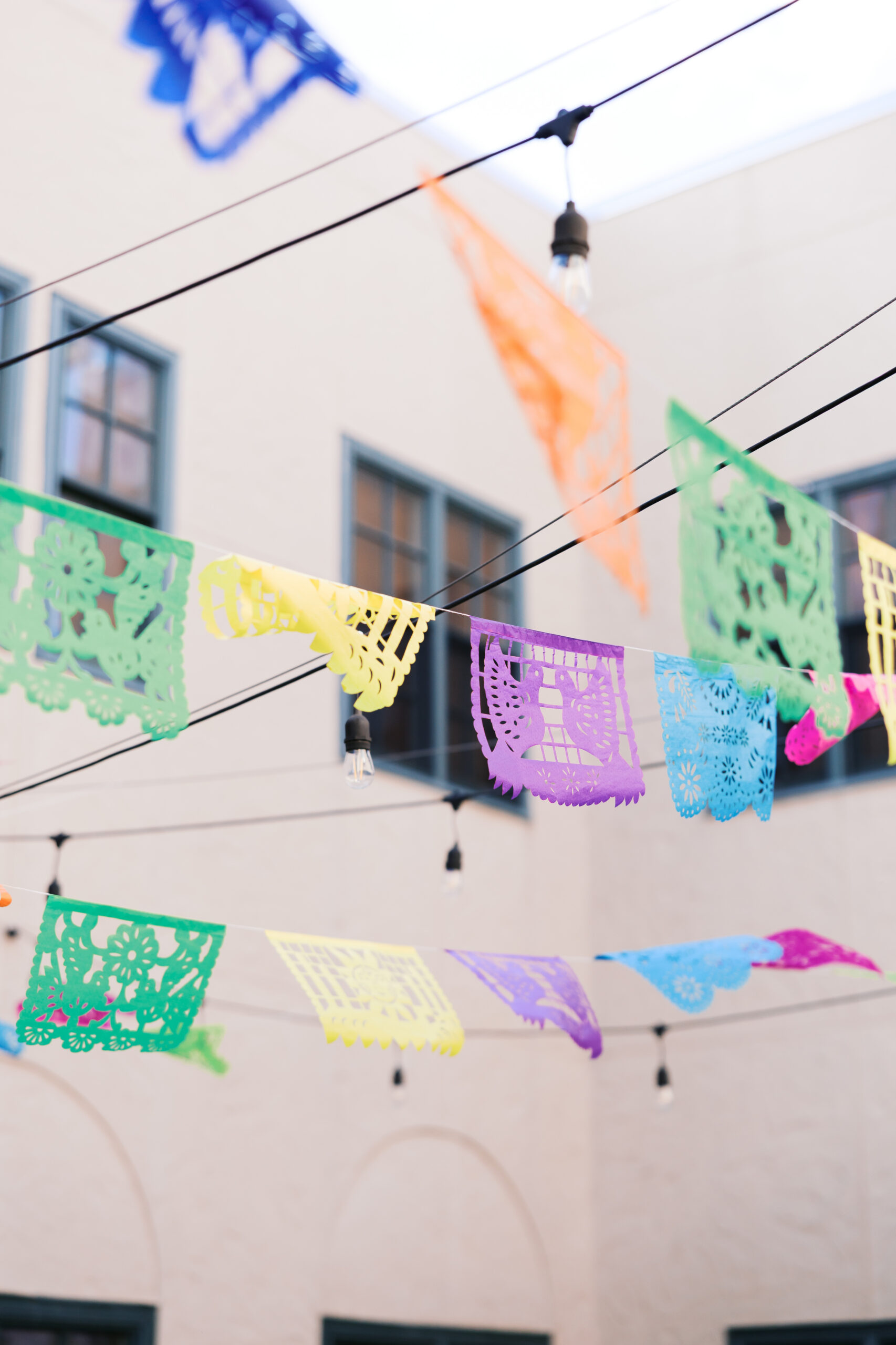 Bright papel picado banners strung overhead with café lights in an outdoor courtyard wedding space.