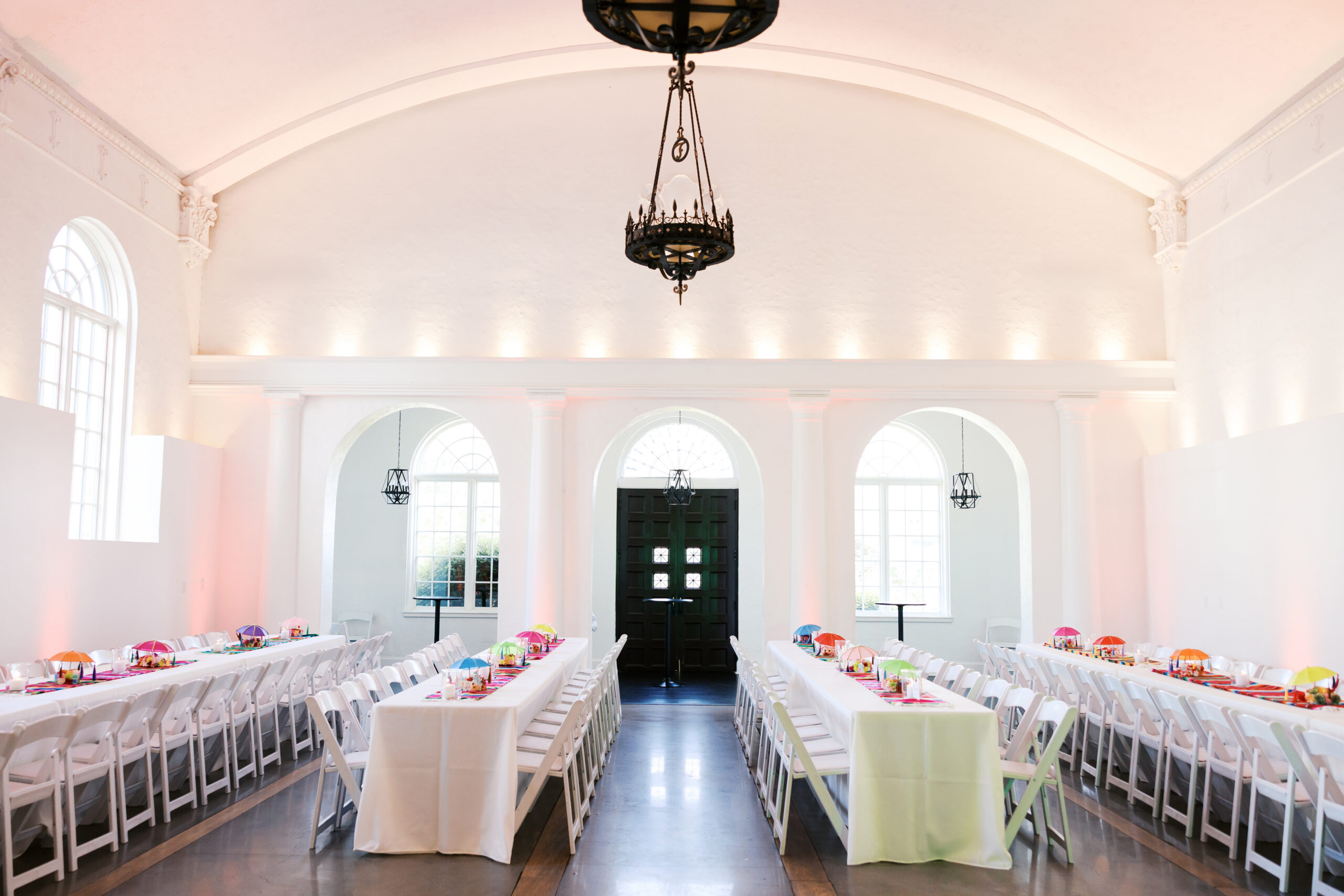 Elegant reception hall with arched windows, chandeliers, and long banquet tables set for a wedding celebration.