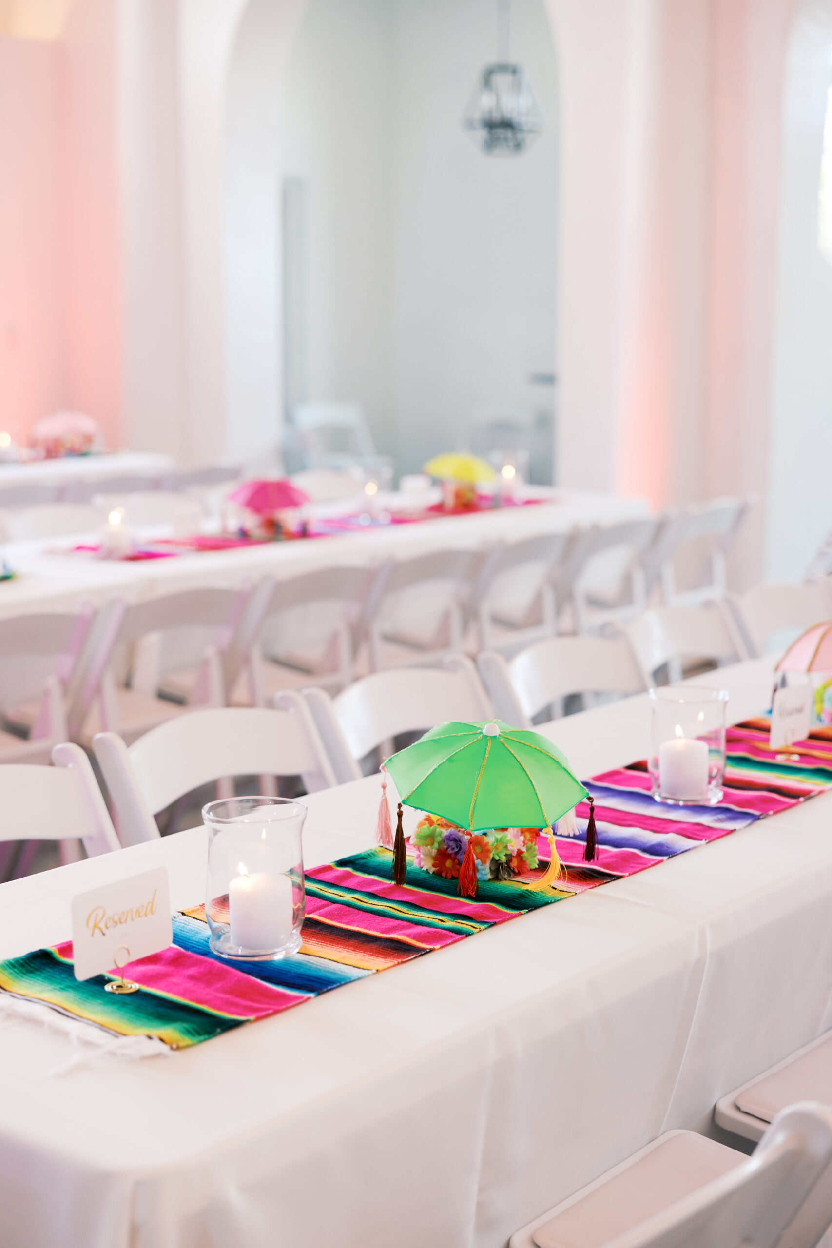 Reception table with bright striped runner, mini umbrella centerpiece, candle, and reserved seating card.
